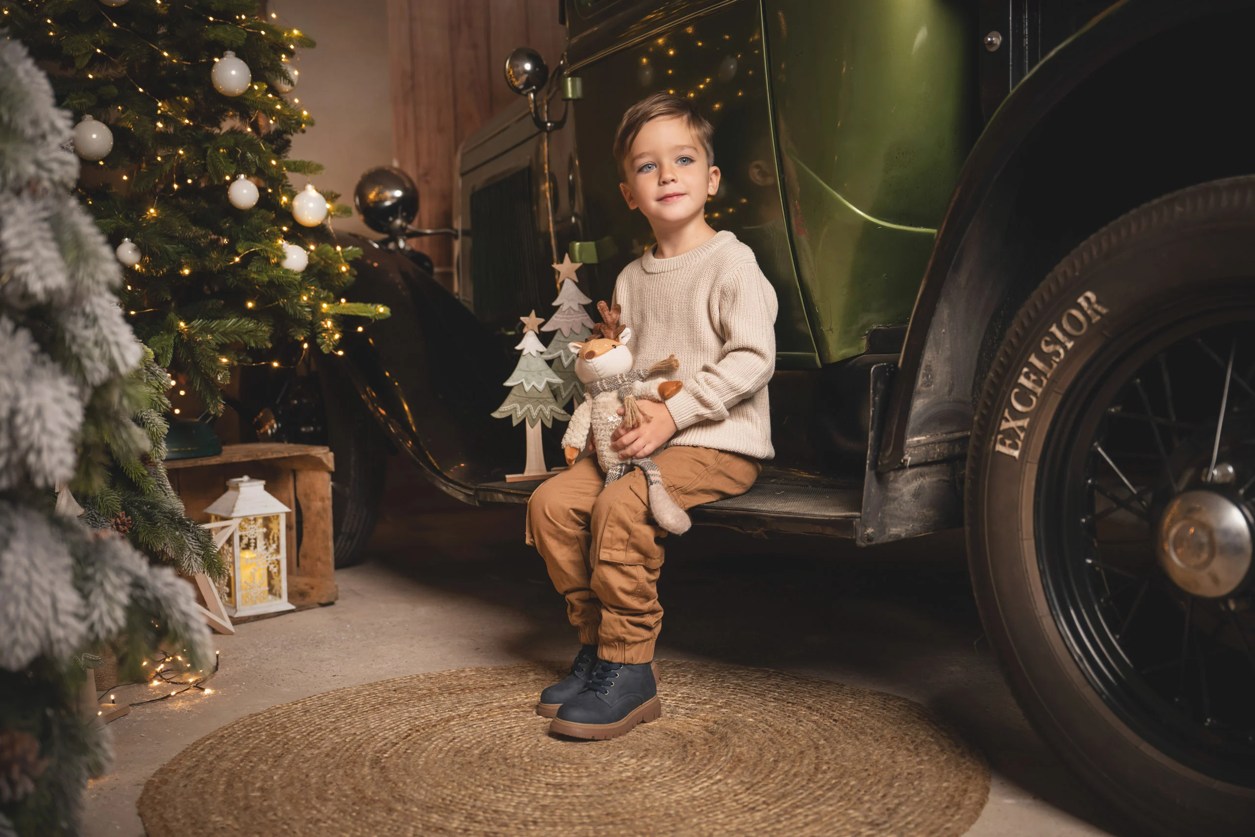 Junge sitzt mit Stofffuchs neben dem großen Reifen des Pick-ups