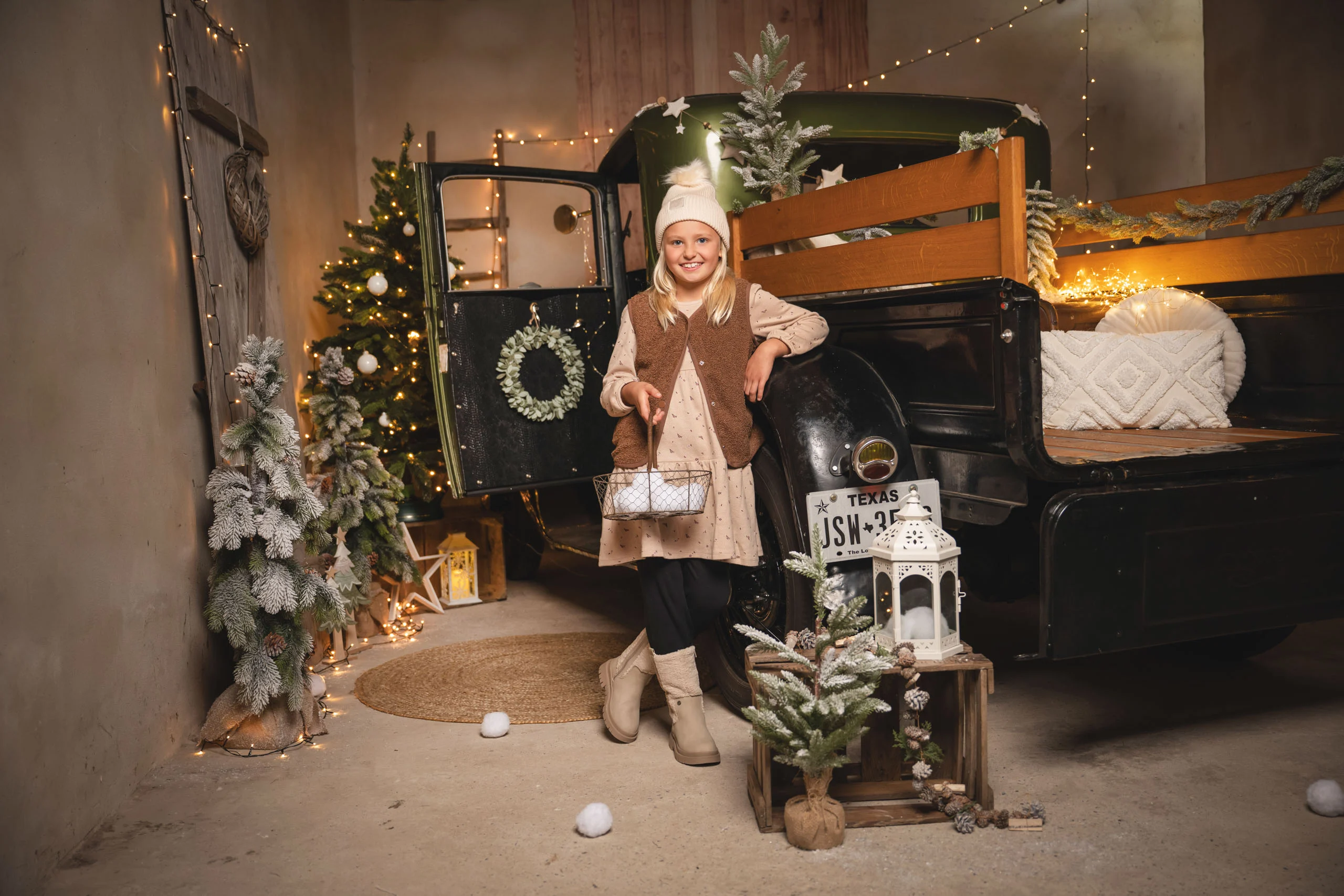 Mädchen mit Bommelmütze steht vor einem geschmückten Pick-up neben einem Weihnachtsbaum