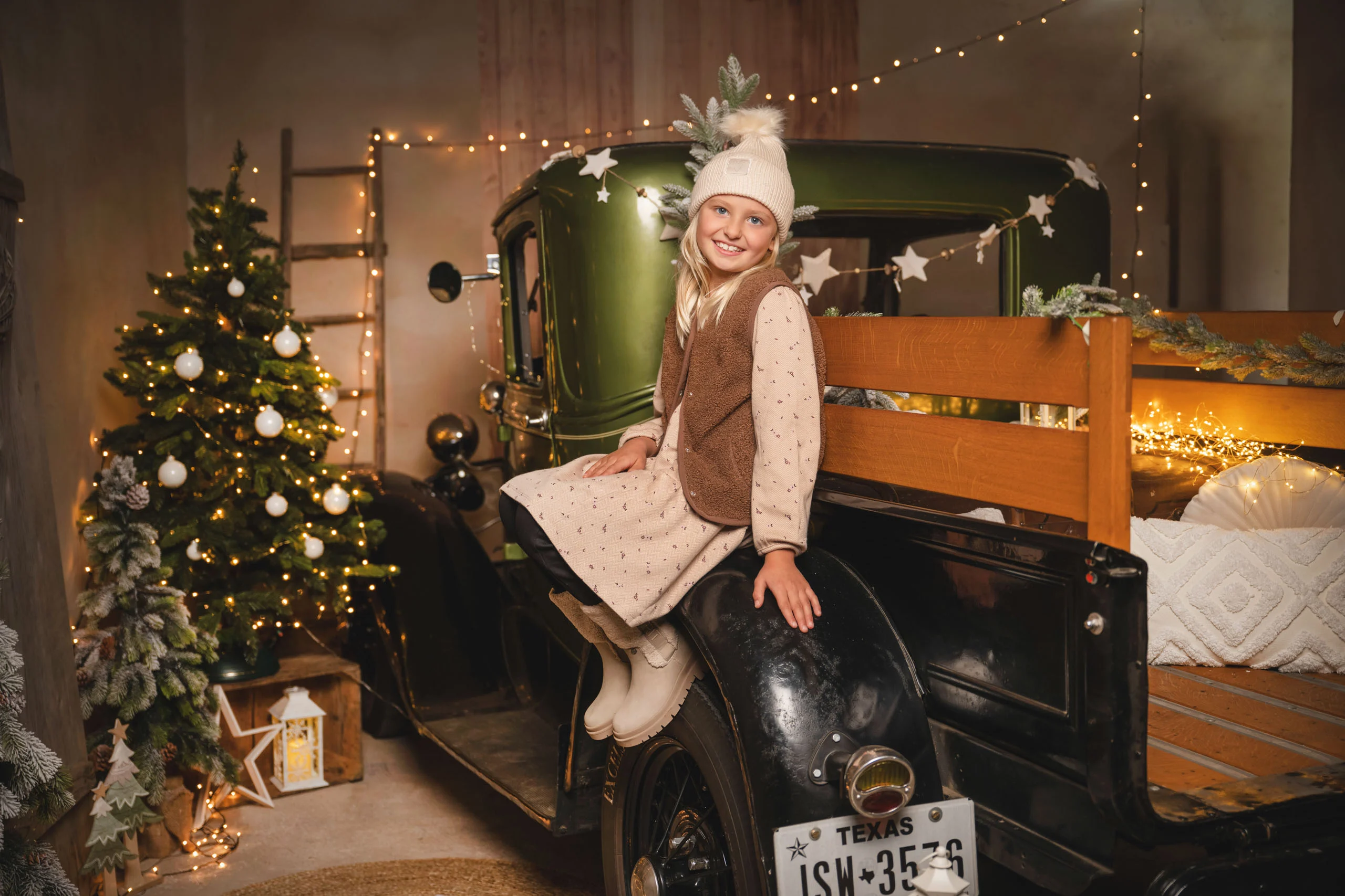 Mädchen sitzt auf dem Kotflügel des Pick-ups vor dem Weihnachtsbaum