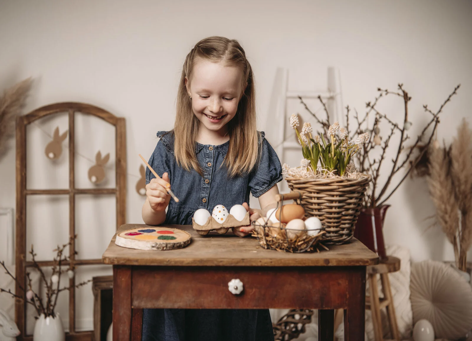 Frühlingshafte Kinderfotos: Mädchen bemalt mit einem Pinsel Ostereier am Holztisch
