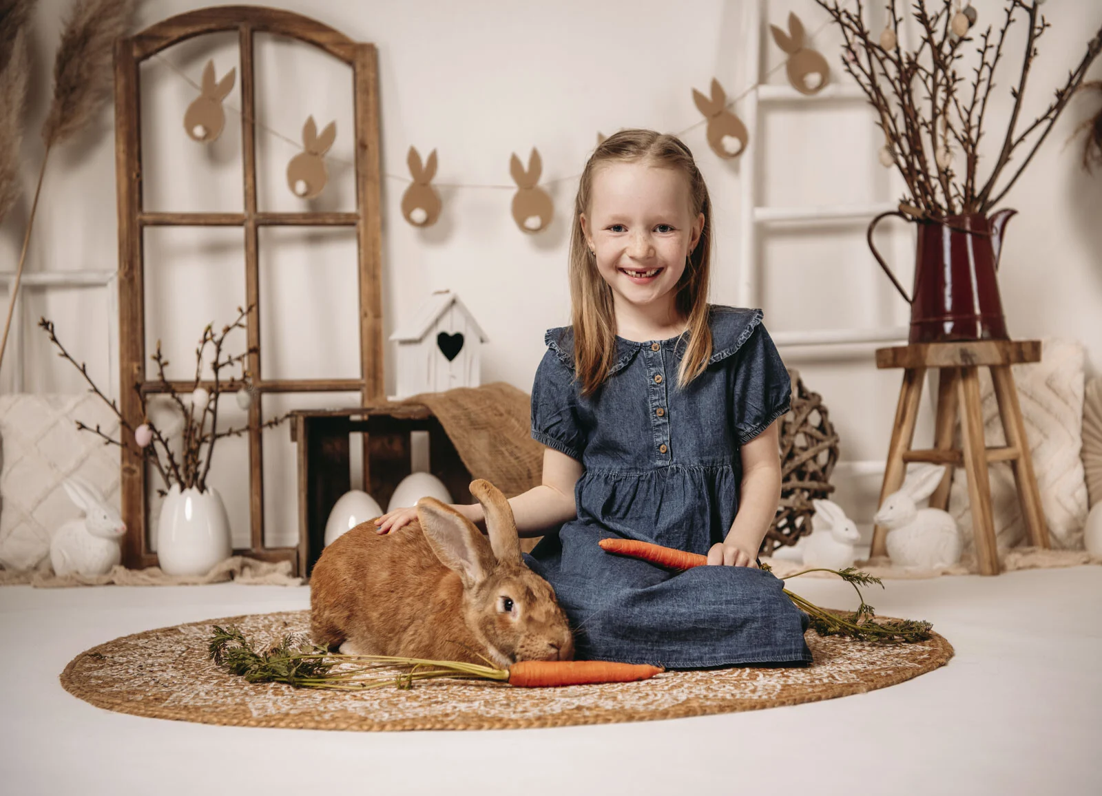 Frühlingshafte Kinderfotos: Mädchen sitzt neben Hoppelhase Hans und hält eine Möhre
