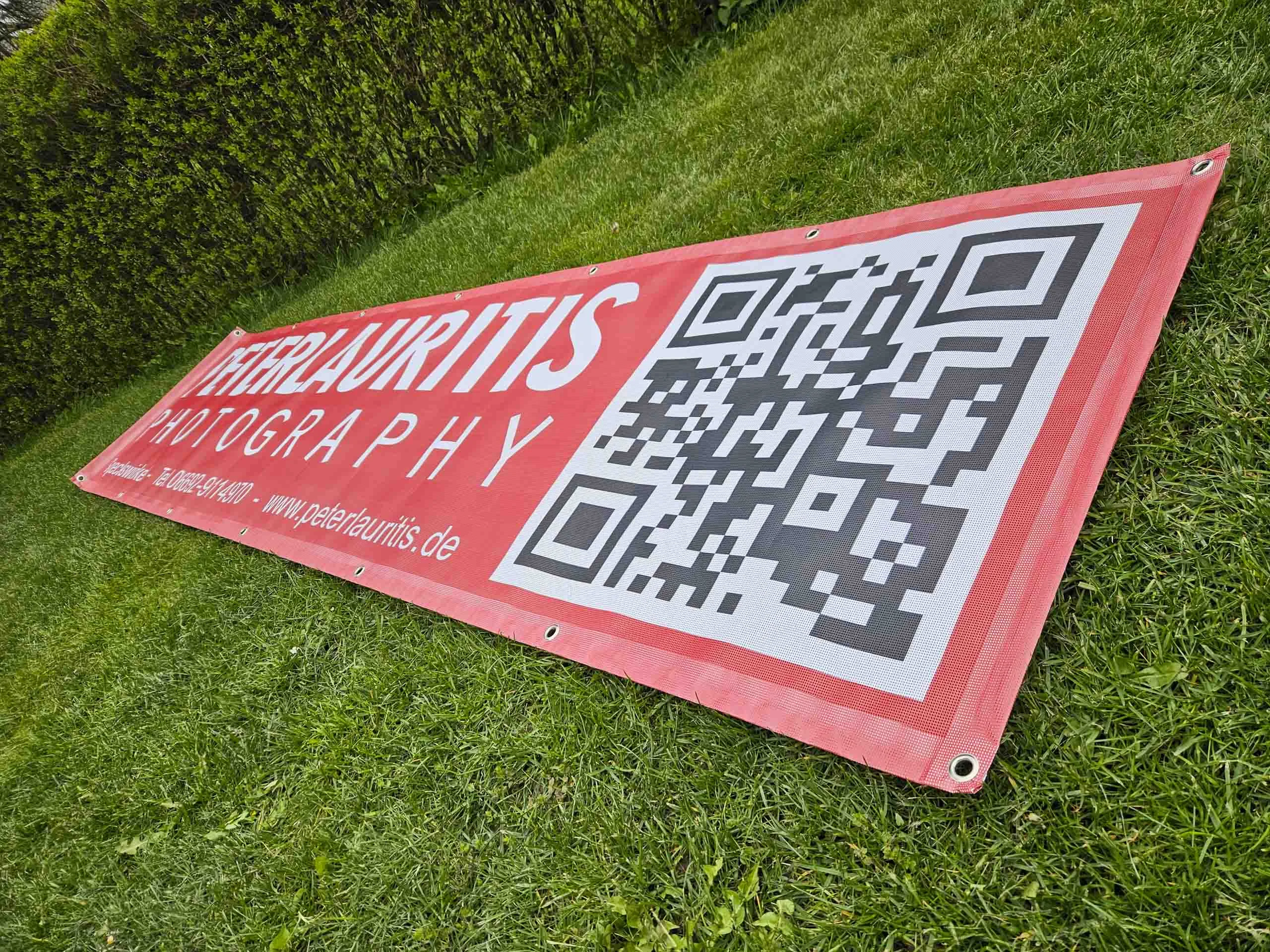 Langes rotes Banner mit großem QR-Code schräg auf einer Wiese