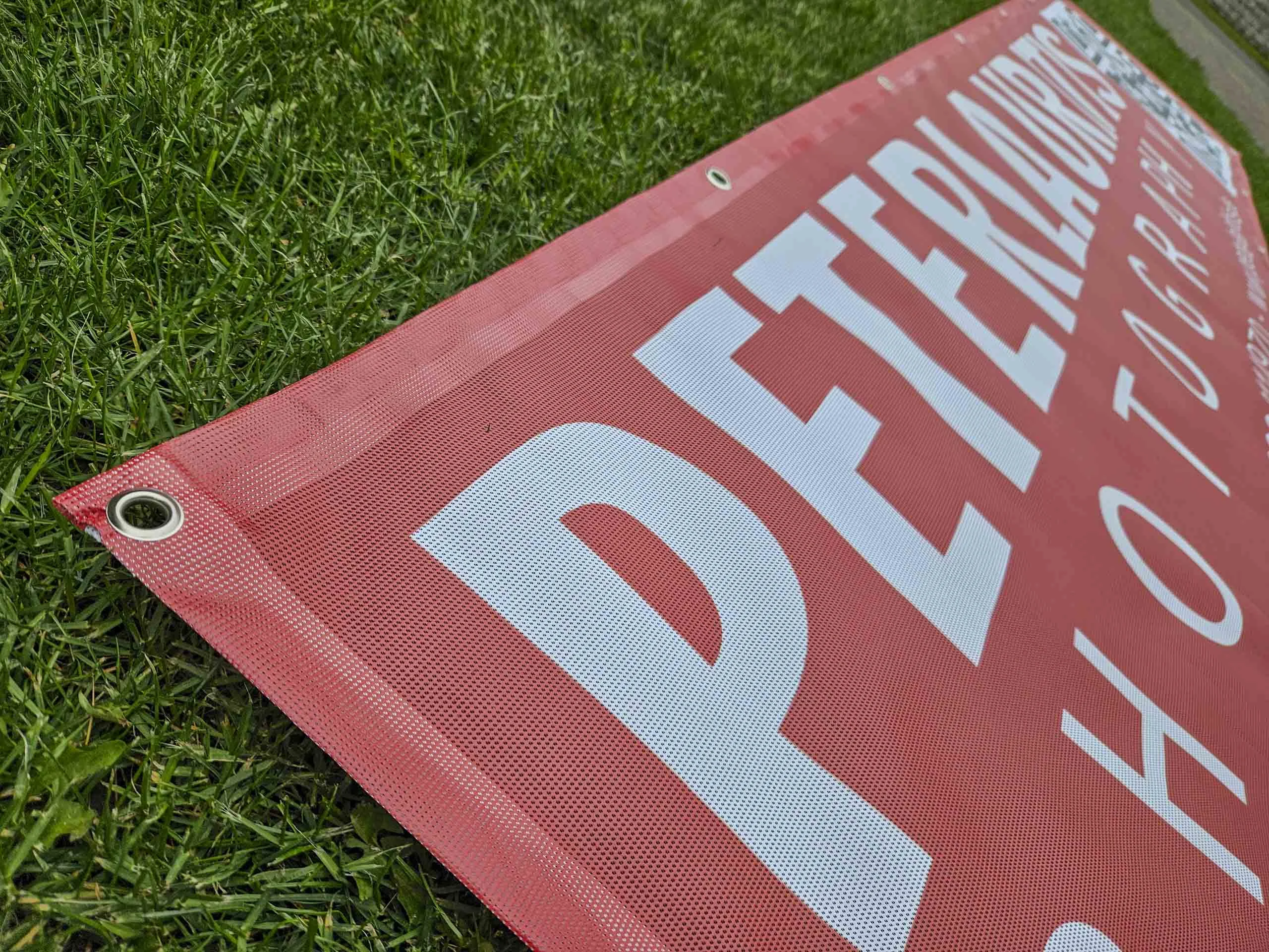 Detail einer Metallöse am Rand eines roten Mesh-Banners