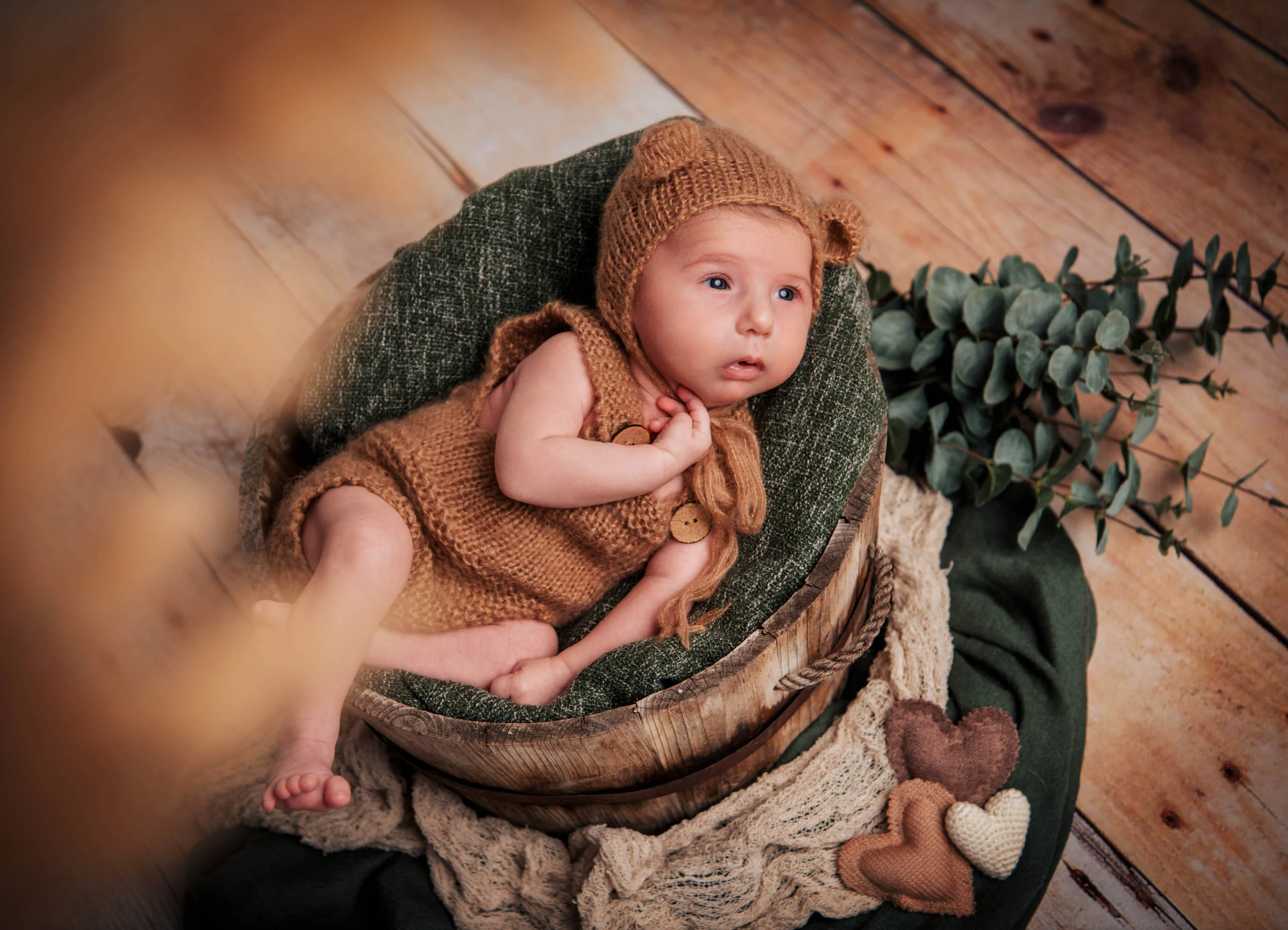 Babyfotos Neugeborene Fotogalerie 009 | Peter Lauritis Photography Baby mit gestrickter Bärenmütze liegt in einer Holzschale auf grüner Decke