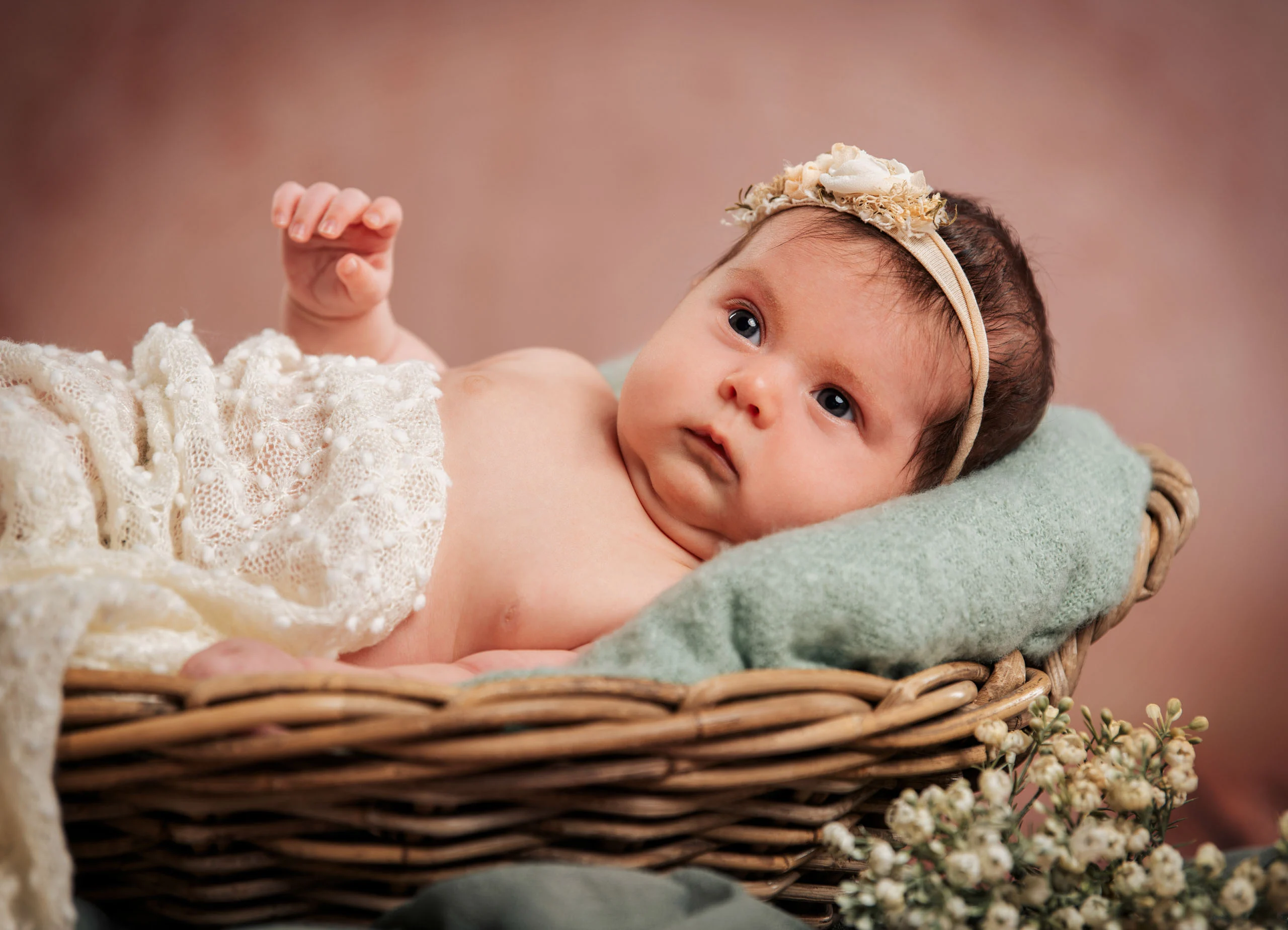 Babyfotos Neugeborene Fotogalerie 011 | Peter Lauritis Photography Baby mit Blumen-Haarband liegt in einem Weidenkorb mit mintgrüner Decke