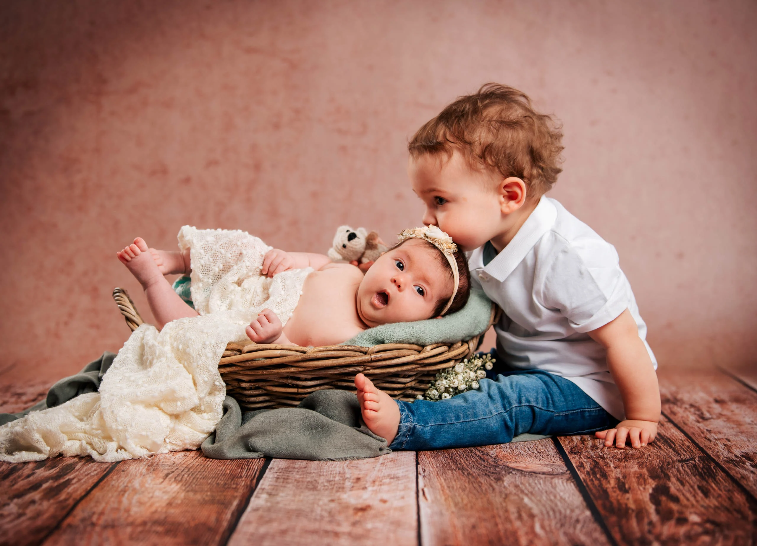 Babyfotos Neugeborene Fotogalerie 012 | Peter Lauritis Photography Kleiner Junge küsst das Baby im Korb vor rosa Hintergrund
