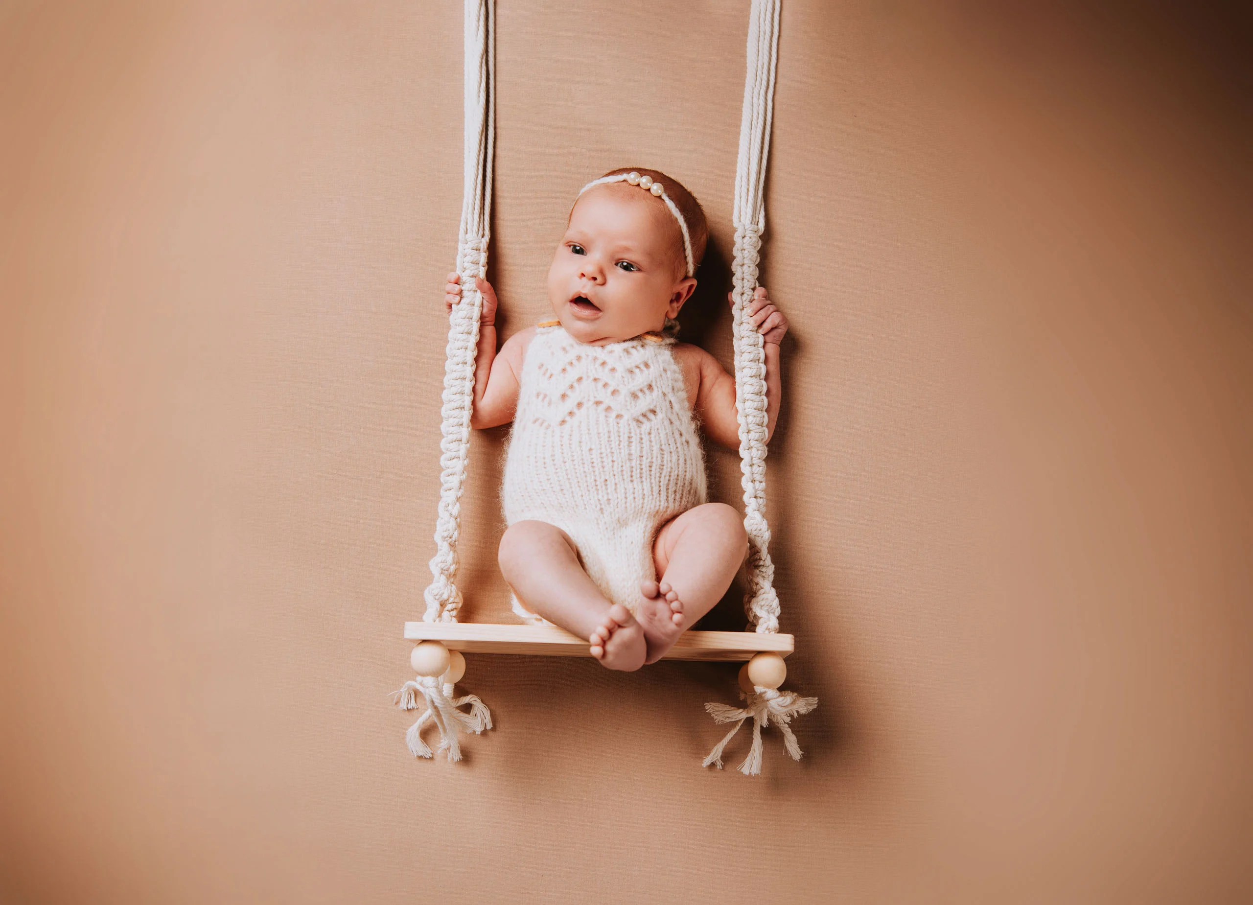 Babyfotos Neugeborene Fotogalerie 013 | Peter Lauritis Photography Baby im Strickbody sitzt auf einer kleinen Makramee-Schaukel
