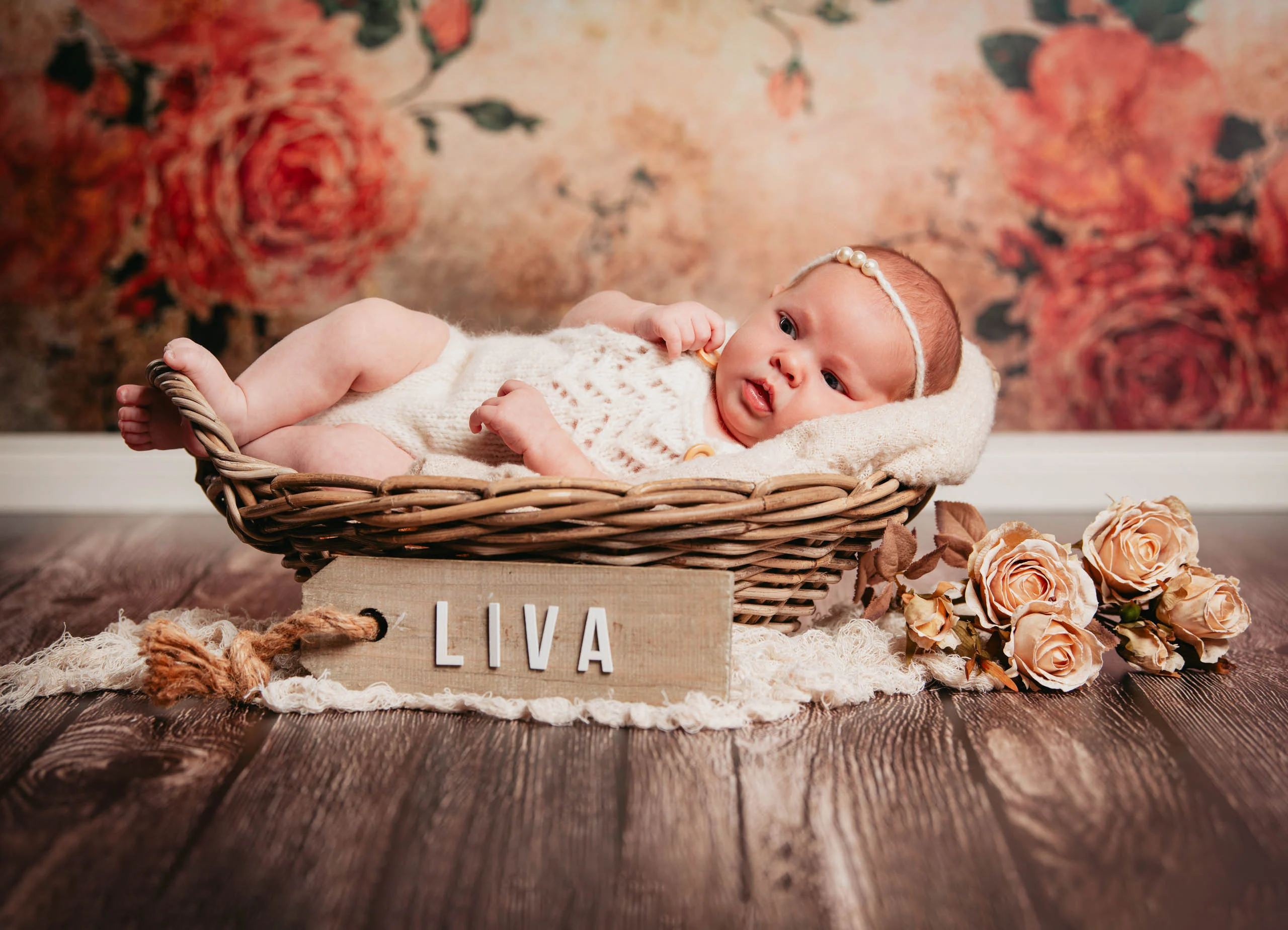 Babyfotos Neugeborene Fotogalerie 015 | Peter Lauritis Photography Baby liegt im Weidenkorb vor Rosentapete, davor ein Holzschild mit Namen