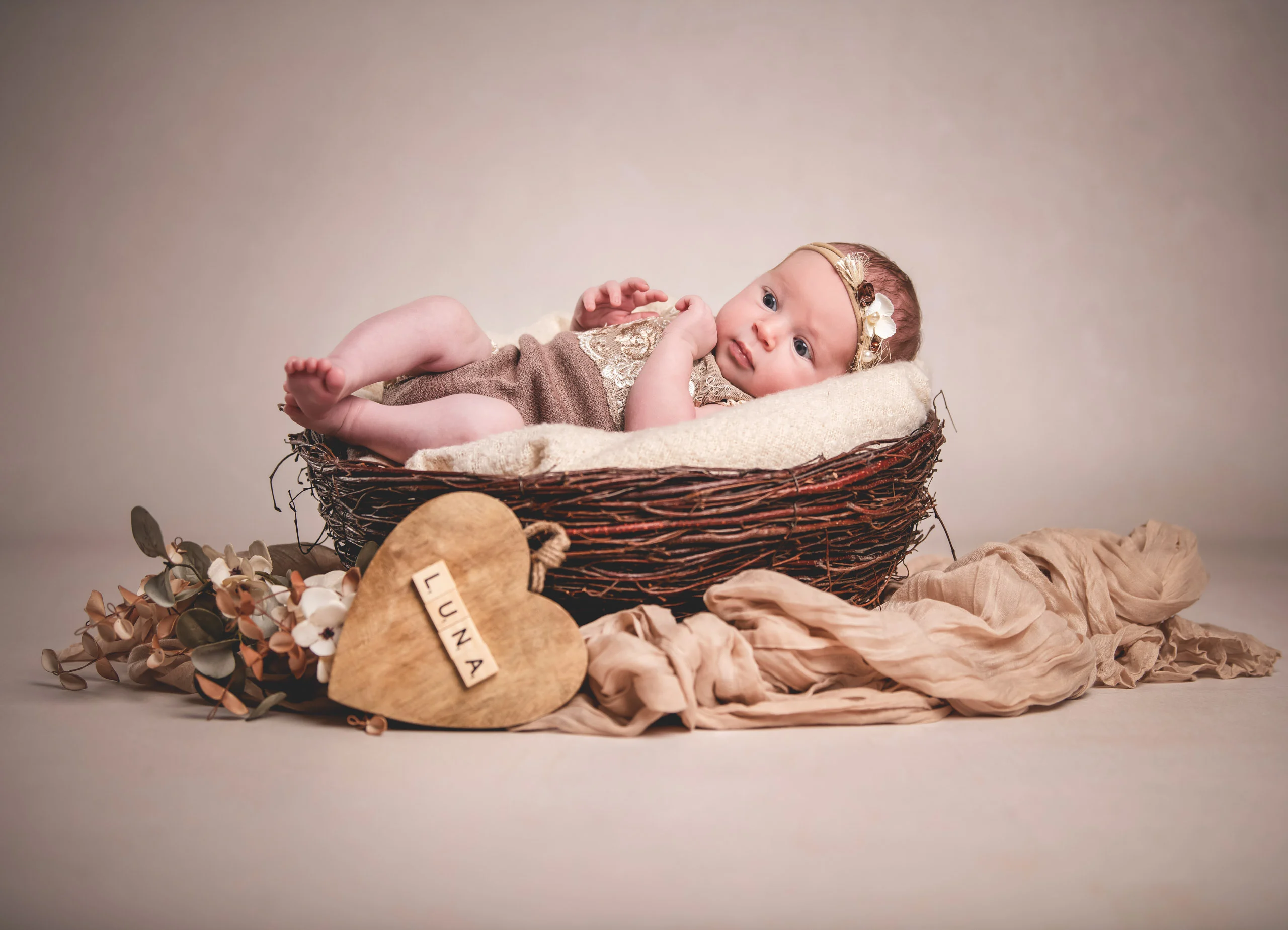 Babyfotos Neugeborene Fotogalerie 017 | Peter Lauritis Photography Baby liegt in einem Nest-Körbchen, davor ein Holzherz mit Namen