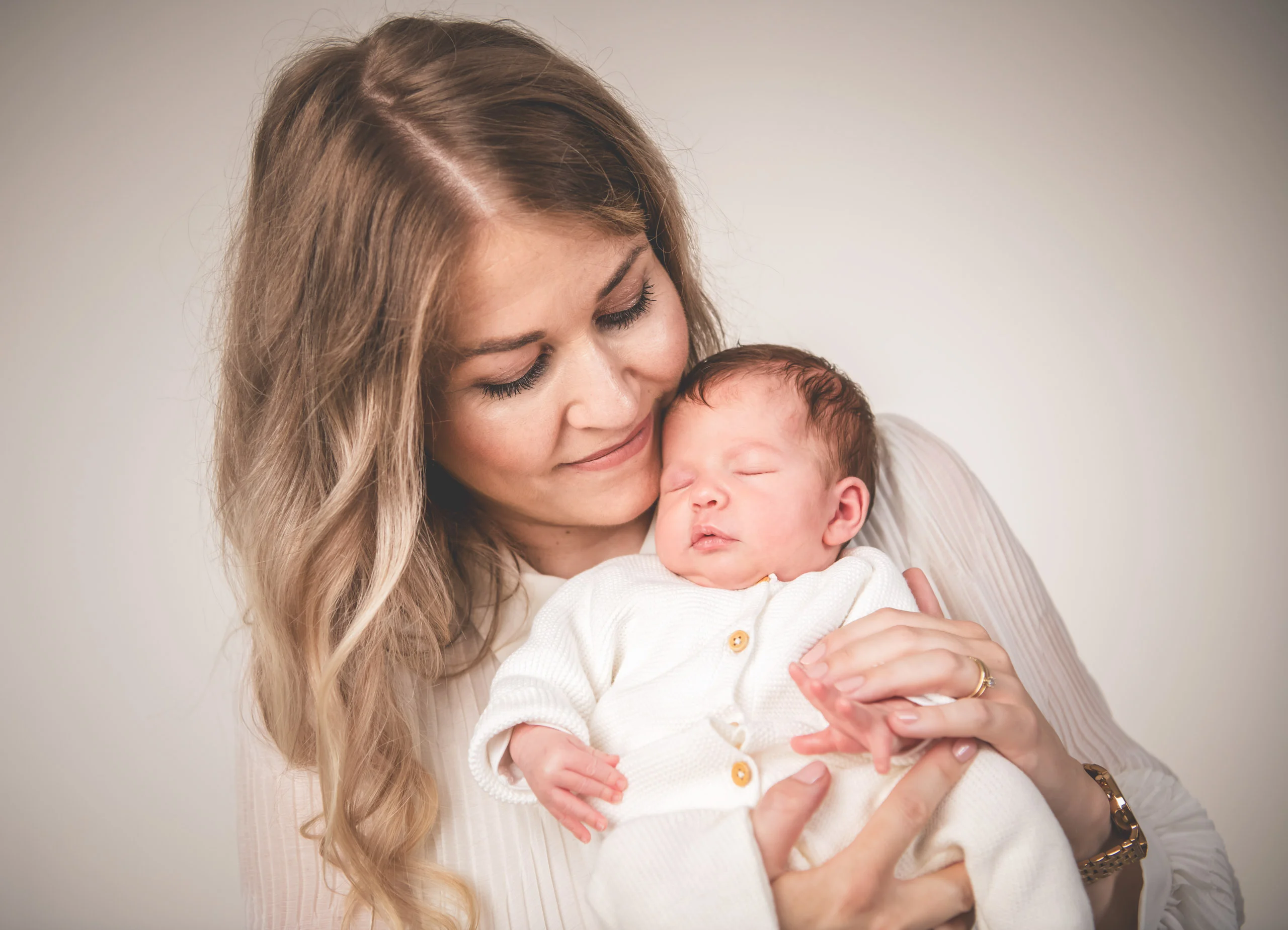 Babyfotos Neugeborene Fotogalerie 018 | Peter Lauritis Photography Frau im weißen Kleid hält ein schlafendes Neugeborenes an ihre Wange