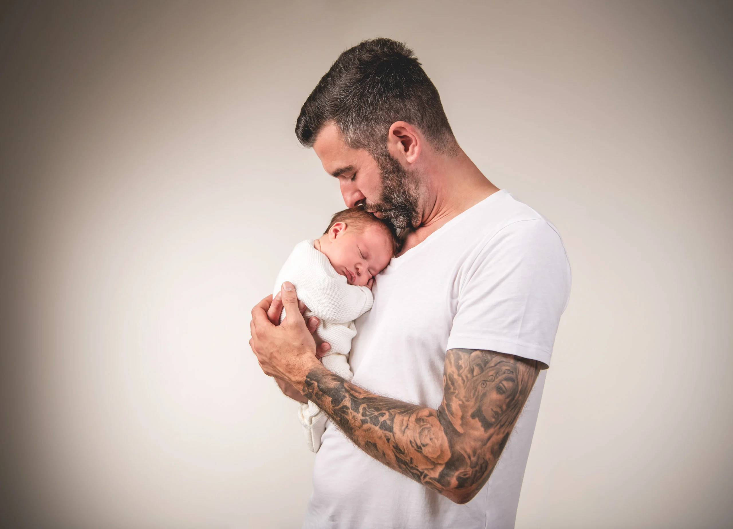 Babyfotos Neugeborene Fotogalerie 019 | Peter Lauritis Photography Tätowierter Mann küsst das schlafende Neugeborene auf seinem Arm