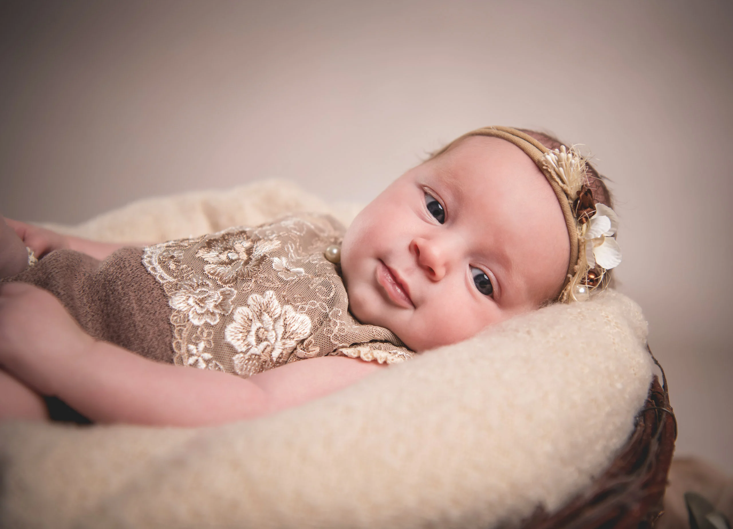 Babyfotos Neugeborene Fotogalerie 021 | Peter Lauritis Photography Baby im Spitzenbody mit Blumen-Haarband liegt lächelnd auf einer Strickdecke