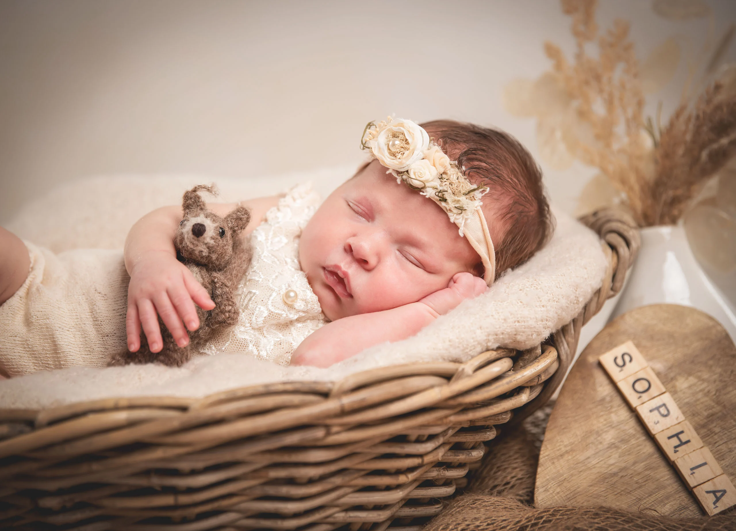 Babyfotos Neugeborene Fotogalerie 023 | Peter Lauritis Photography Schlafendes Neugeborenes mit Blumen-Haarband und Strickteddy im Weidenkorb