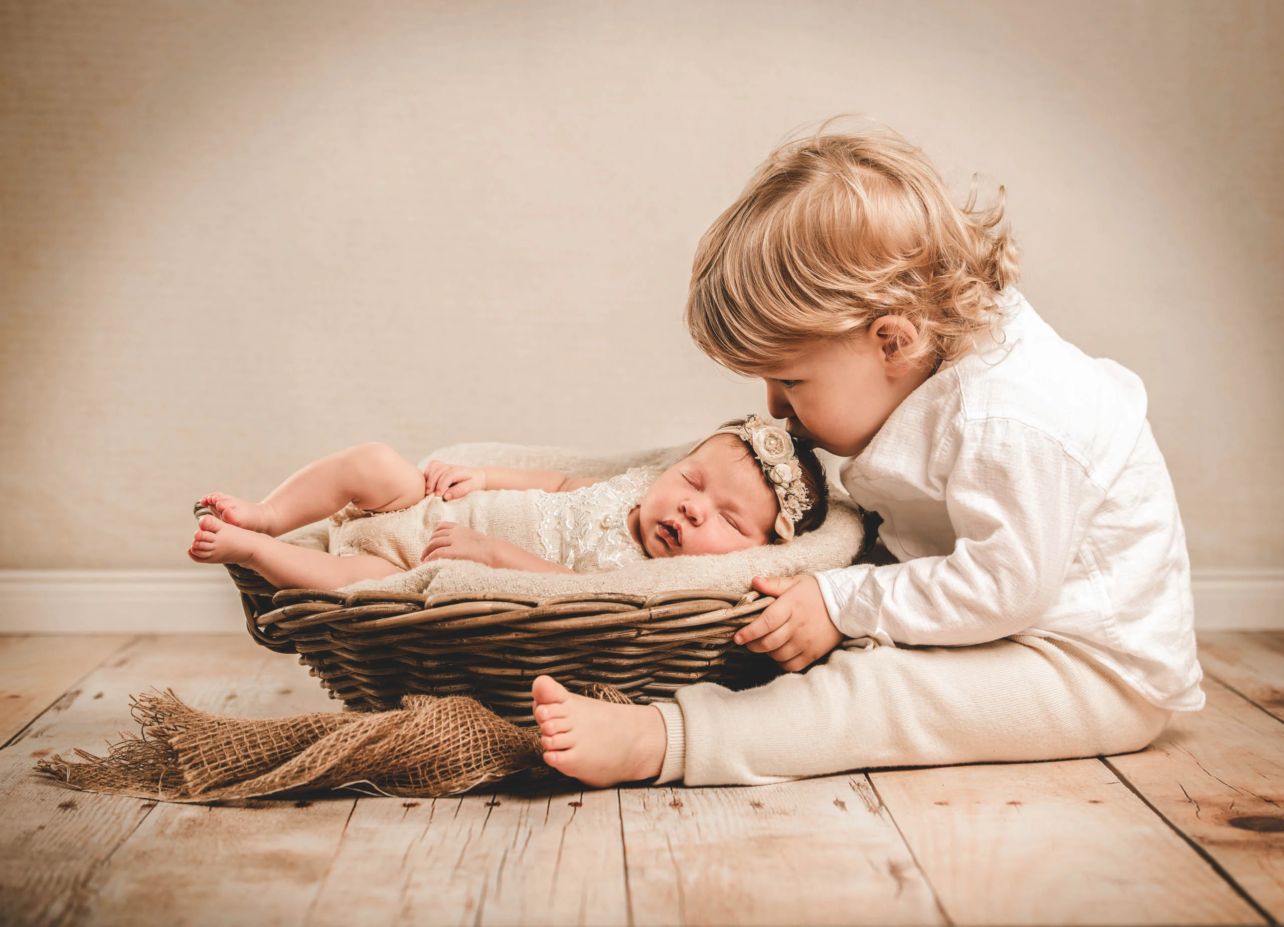 Babyfotos Neugeborene Fotogalerie 024 | Peter Lauritis Photography Kleiner Junge in Weiß küsst das Neugeborene im Korb auf Holzboden