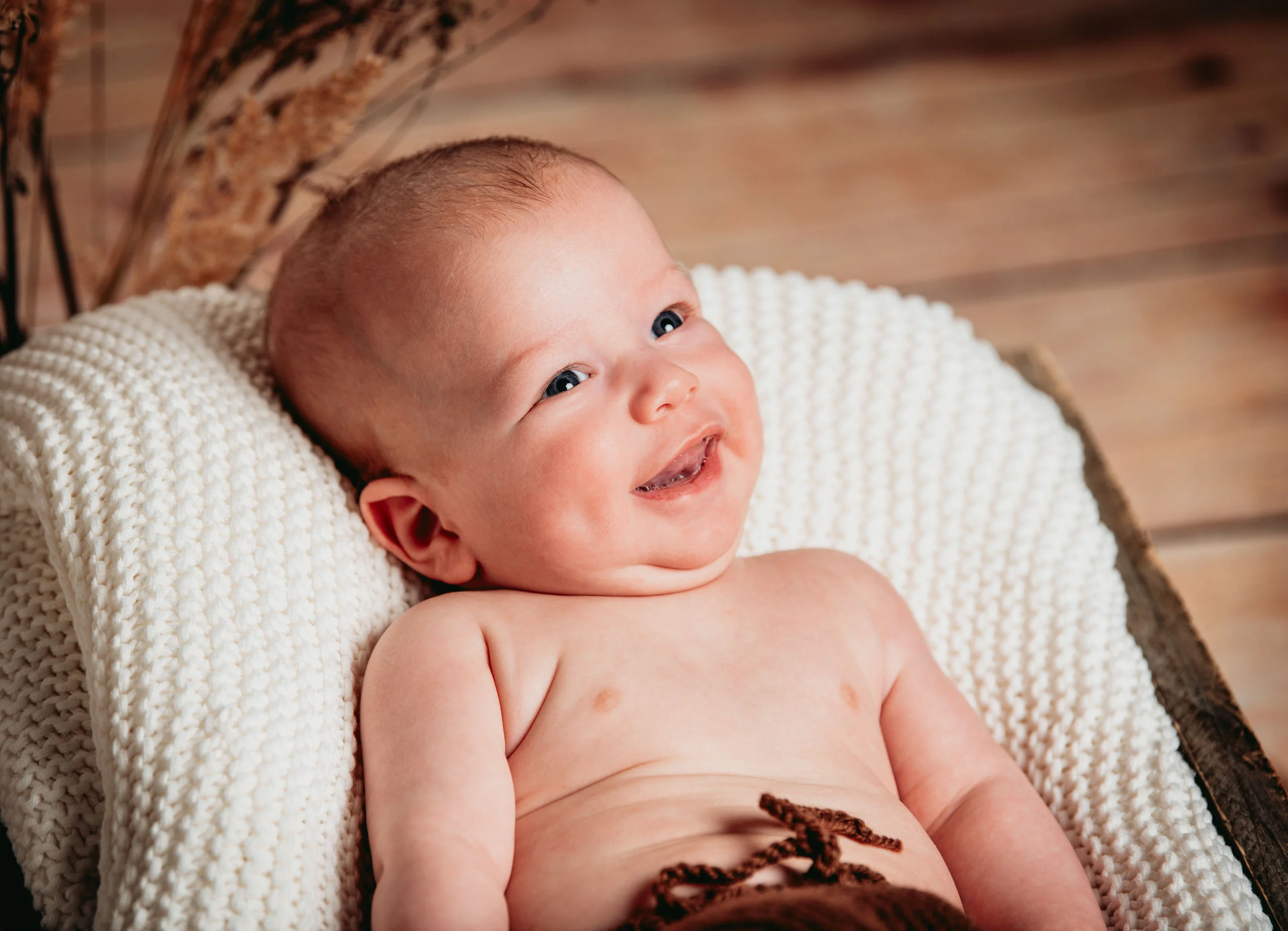 Babyfotos Neugeborene Fotogalerie 025 | Peter Lauritis Photography Lachendes Baby liegt auf einer weißen Strickdecke in einer Holzkiste