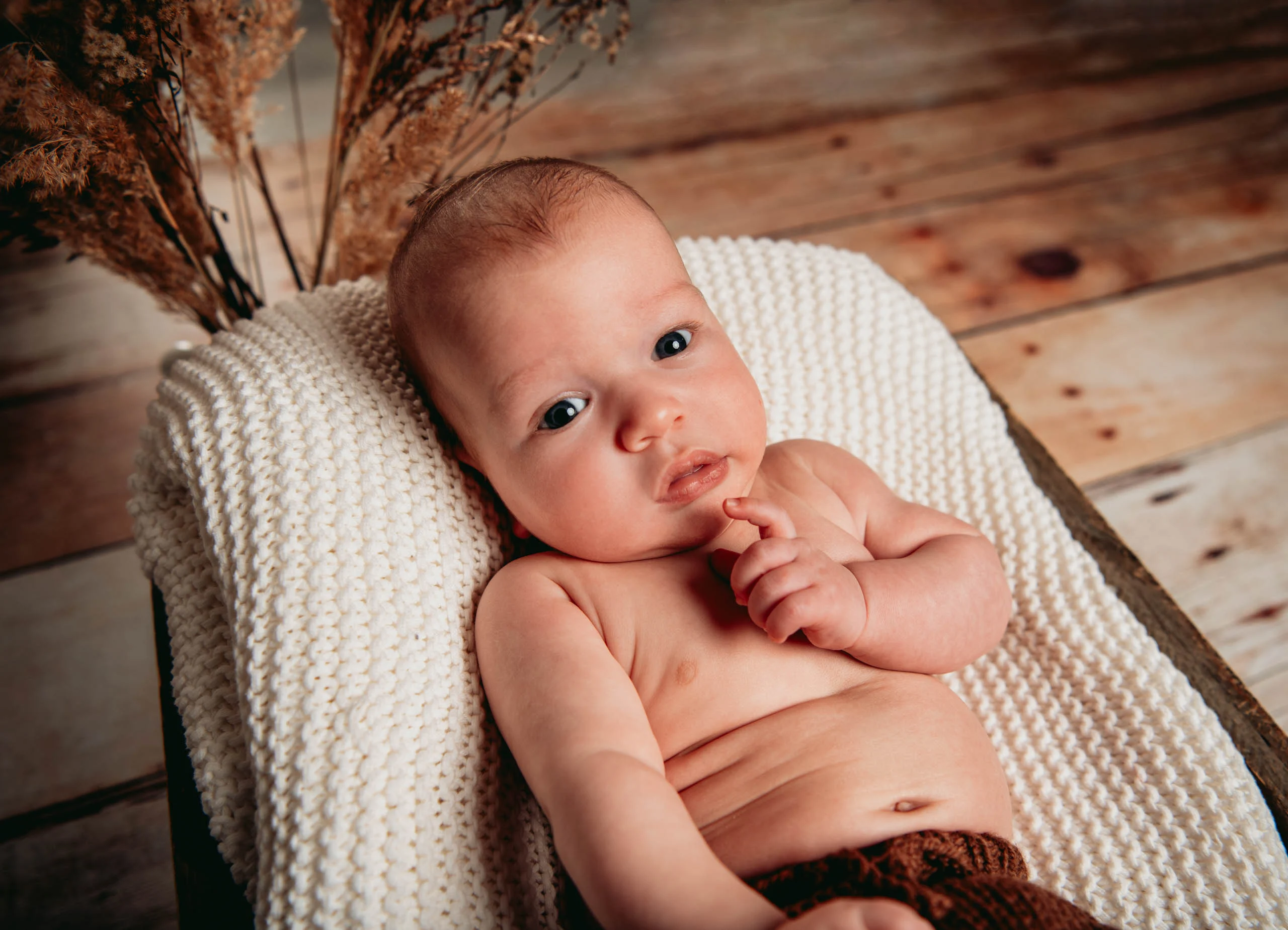 Babyfotos Neugeborene Fotogalerie 026 | Peter Lauritis Photography Baby nuckelt an der Hand und liegt auf einer Strickdecke vor Holzwand