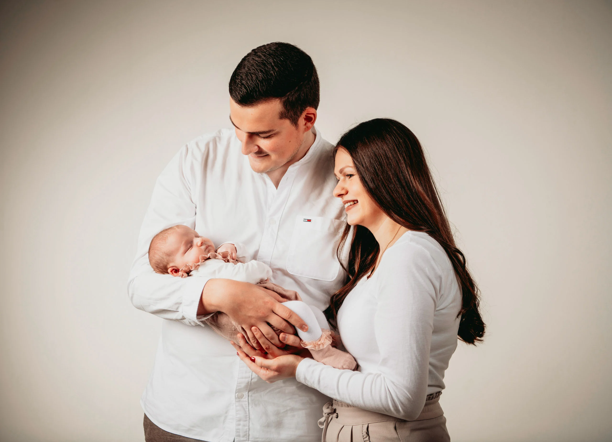 Babyfotos Neugeborene Fotogalerie 028 | Peter Lauritis Photography Eltern in Weiß halten ihr Neugeborenes und lächeln es an