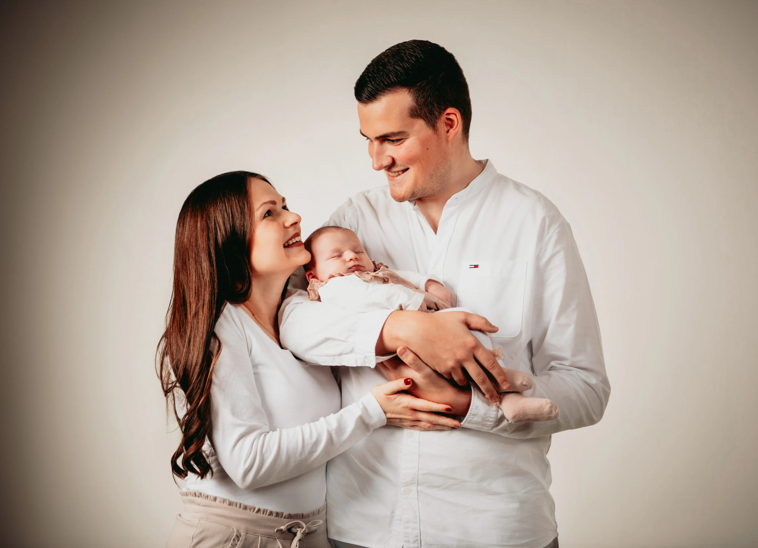 Babyfotos Neugeborene Fotogalerie 029 | Peter Lauritis Photography Mann hält das Neugeborene im Arm, die Frau schmiegt sich lächelnd an