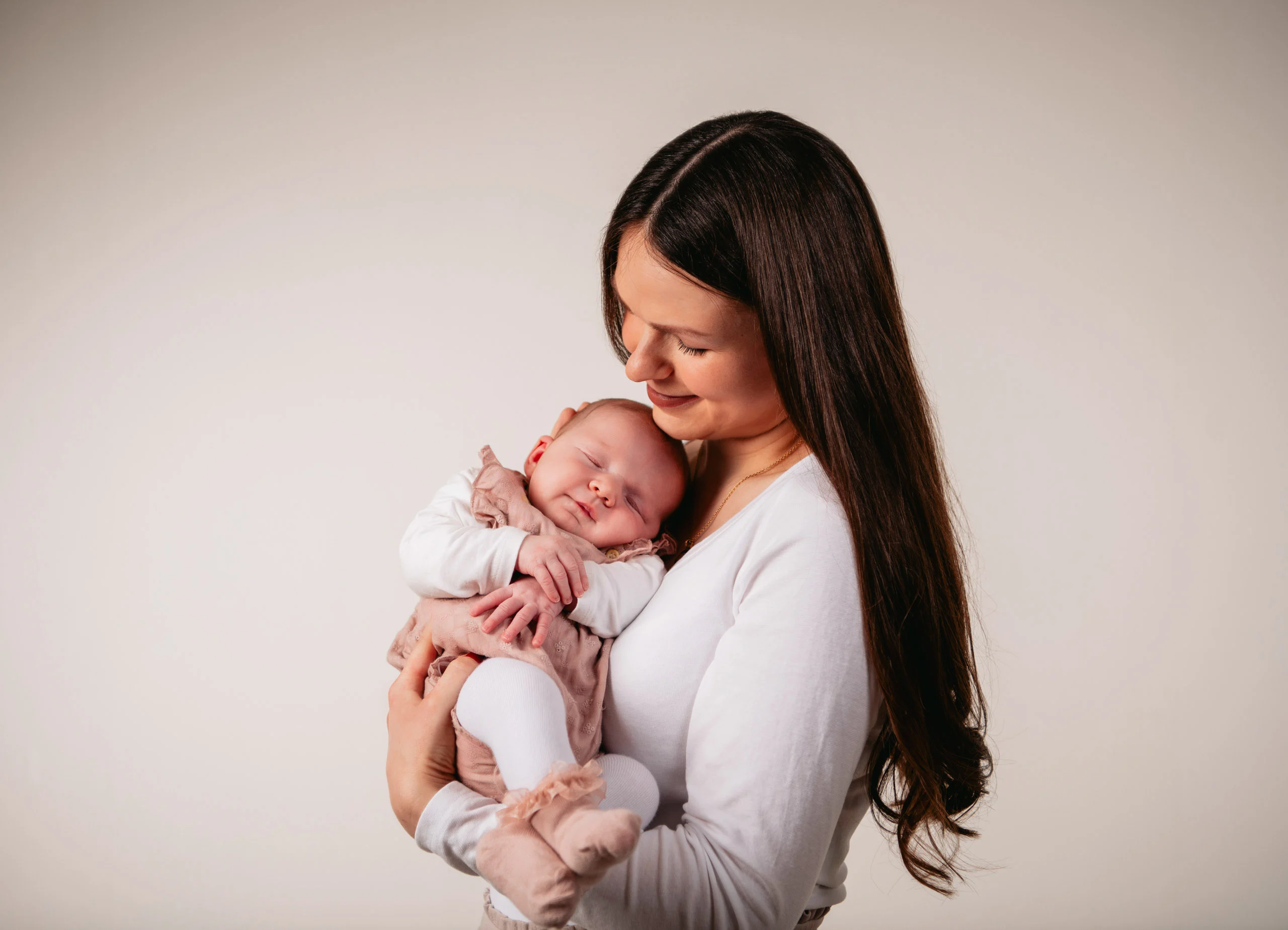 Babyfotos Neugeborene Fotogalerie 030 | Peter Lauritis Photography Frau mit langen dunklen Haaren hält ihr schlafendes Baby an der Brust