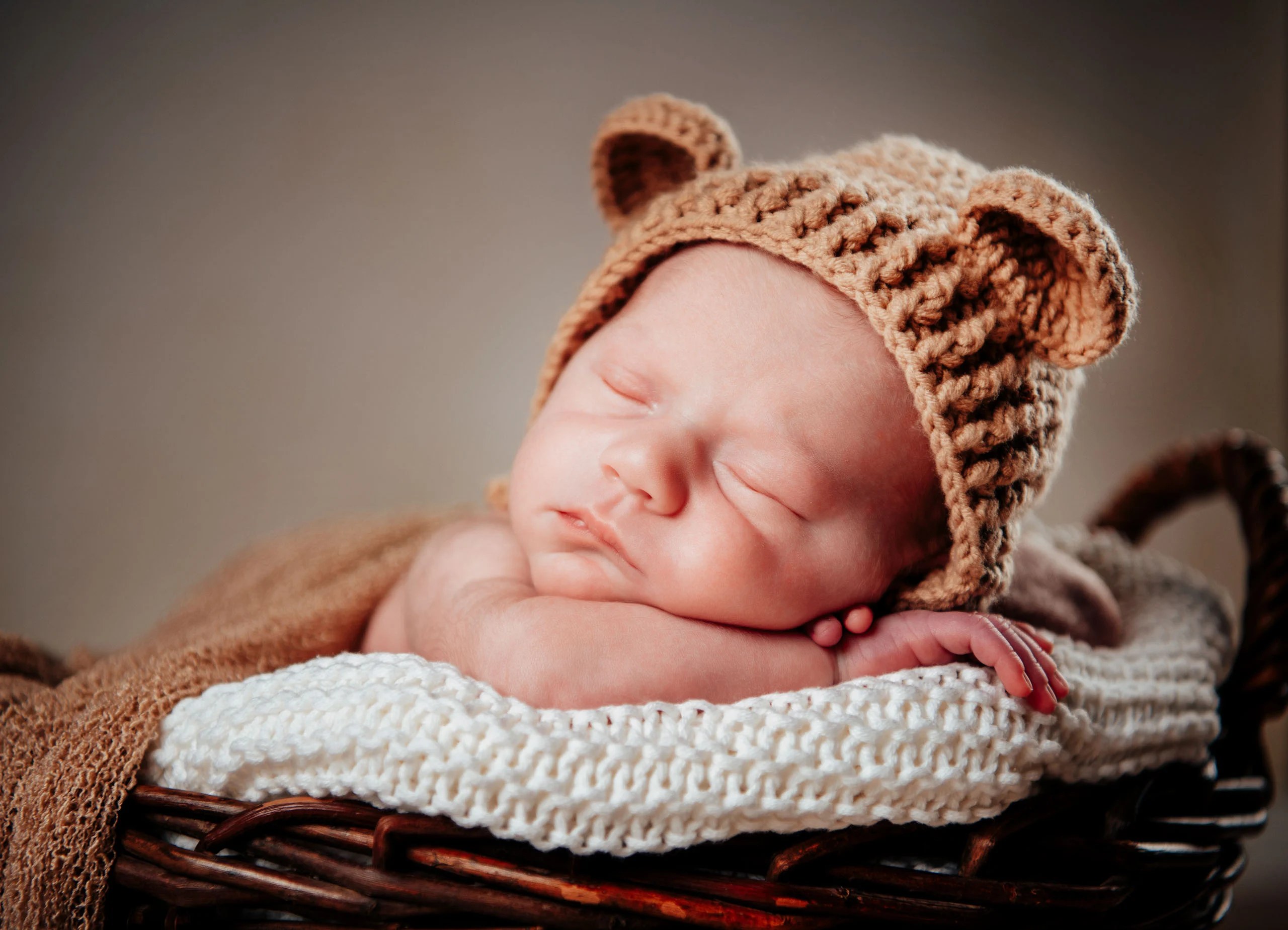 Babyfotos Neugeborene Fotogalerie 038 | Peter Lauritis Photography Neugeborenes mit Bärenmütze schläft auf den Händen im Korb