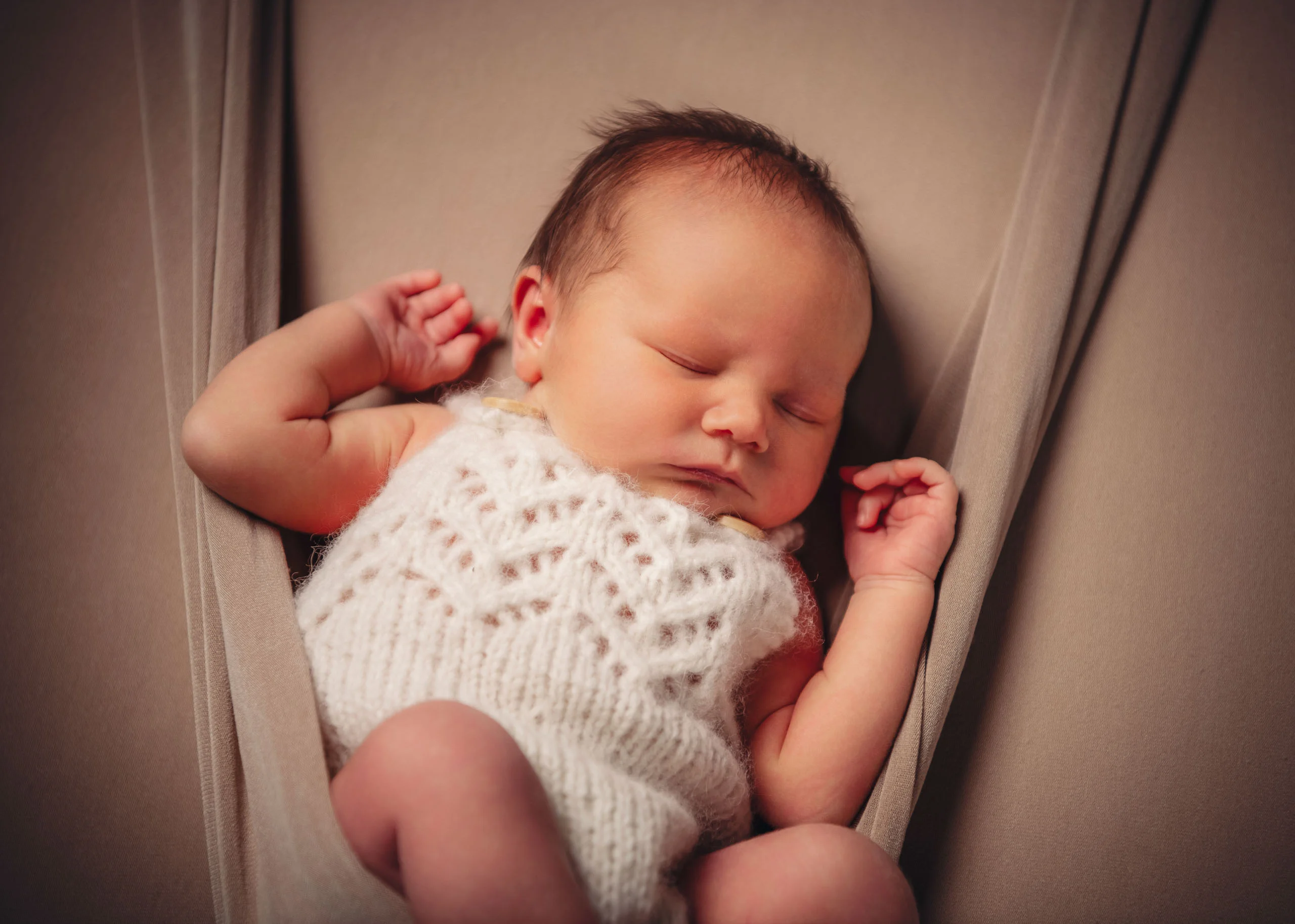 Babyfotos Neugeborene Fotogalerie 045 | Peter Lauritis Photography Neugeborenes im weißen Strickbody schläft in einer Stoffhängematte