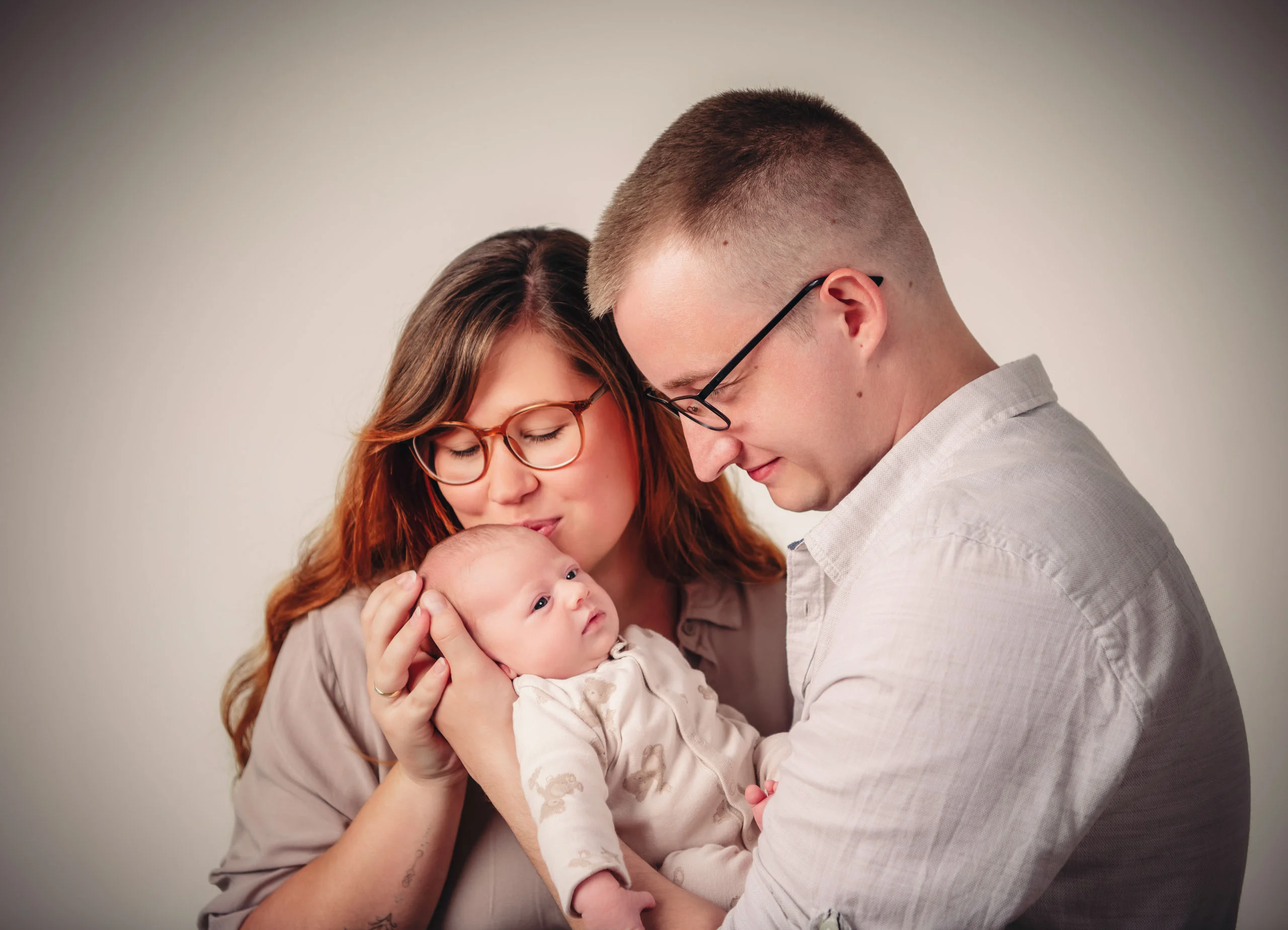 Babyfotos Neugeborene Fotogalerie 050 | Peter Lauritis Photography Paar mit Brillen kuschelt sein Neugeborenes zwischen sich