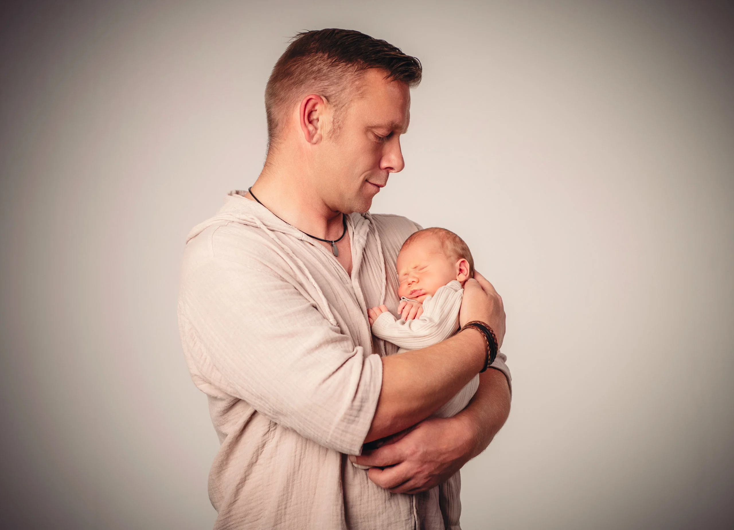 Babyfotos Neugeborene Fotogalerie 051 | Peter Lauritis Photography Mann im Leinenhemd hält das schlafende Neugeborene an der Brust