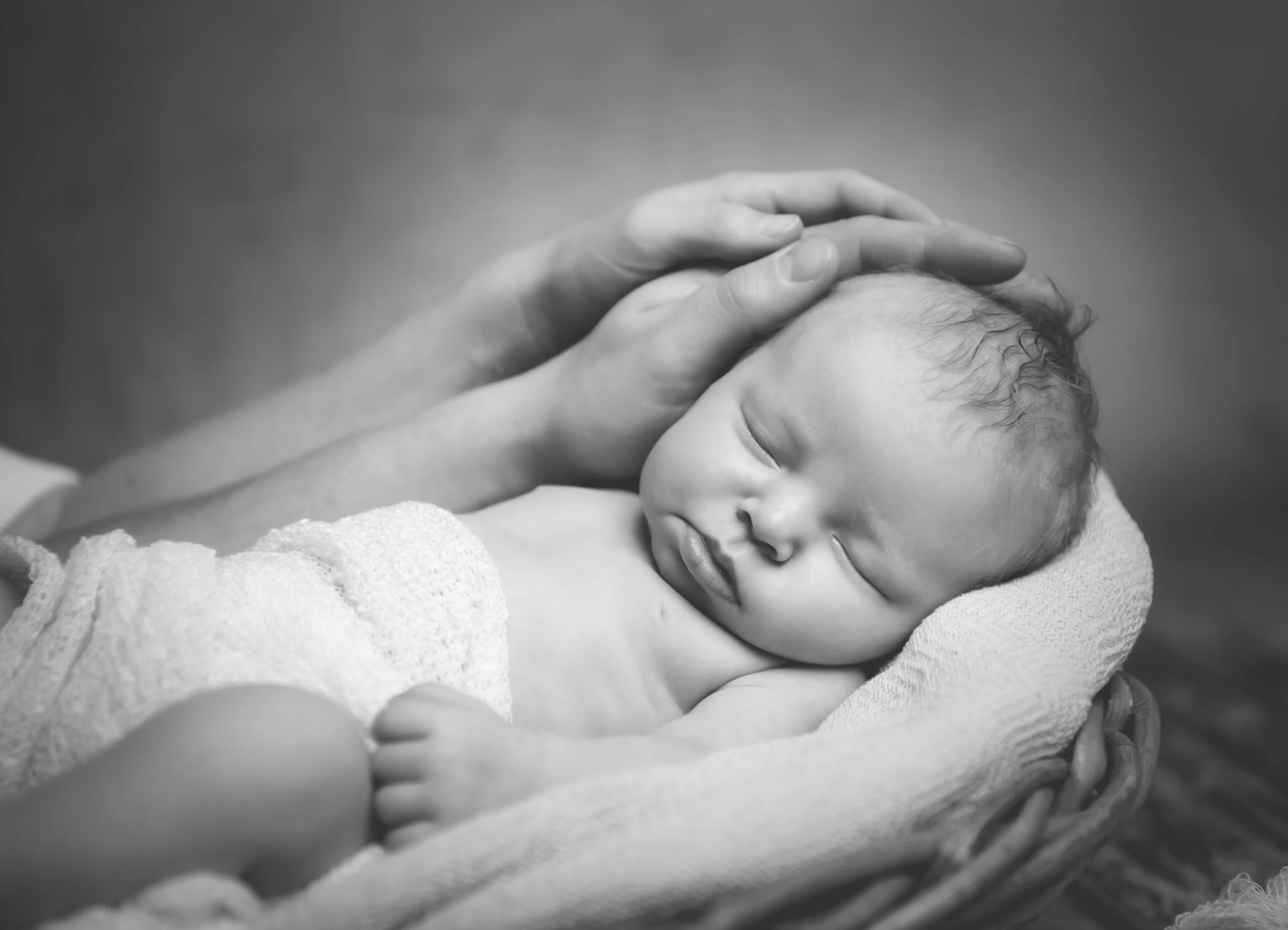 Babyfotos Neugeborene Fotogalerie 054 | Peter Lauritis Photography Schwarzweißfoto: Hände streicheln den Kopf eines schlafenden Neugeborenen