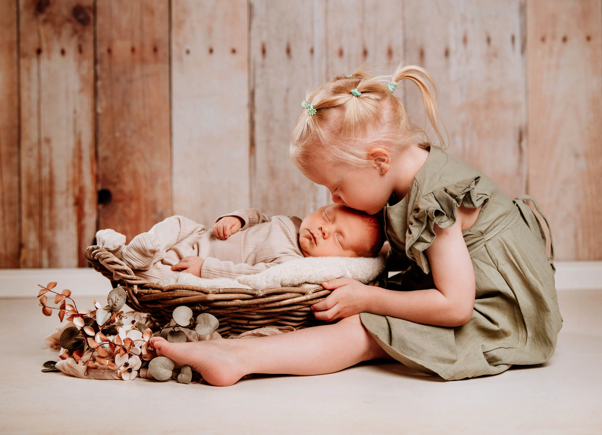 Babyfotos Neugeborene Fotogalerie 058 | Peter Lauritis Photography Kleines Mädchen küsst das Neugeborene im Korb vor Holzwand