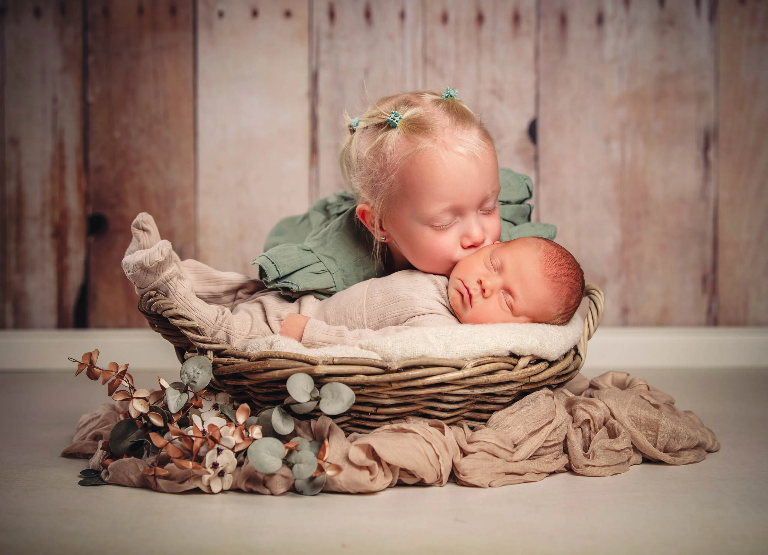 Babyfotos Neugeborene Fotogalerie 061 | Peter Lauritis Photography Kleinkind küsst das schlafende Neugeborene im Korb vor Holzwand