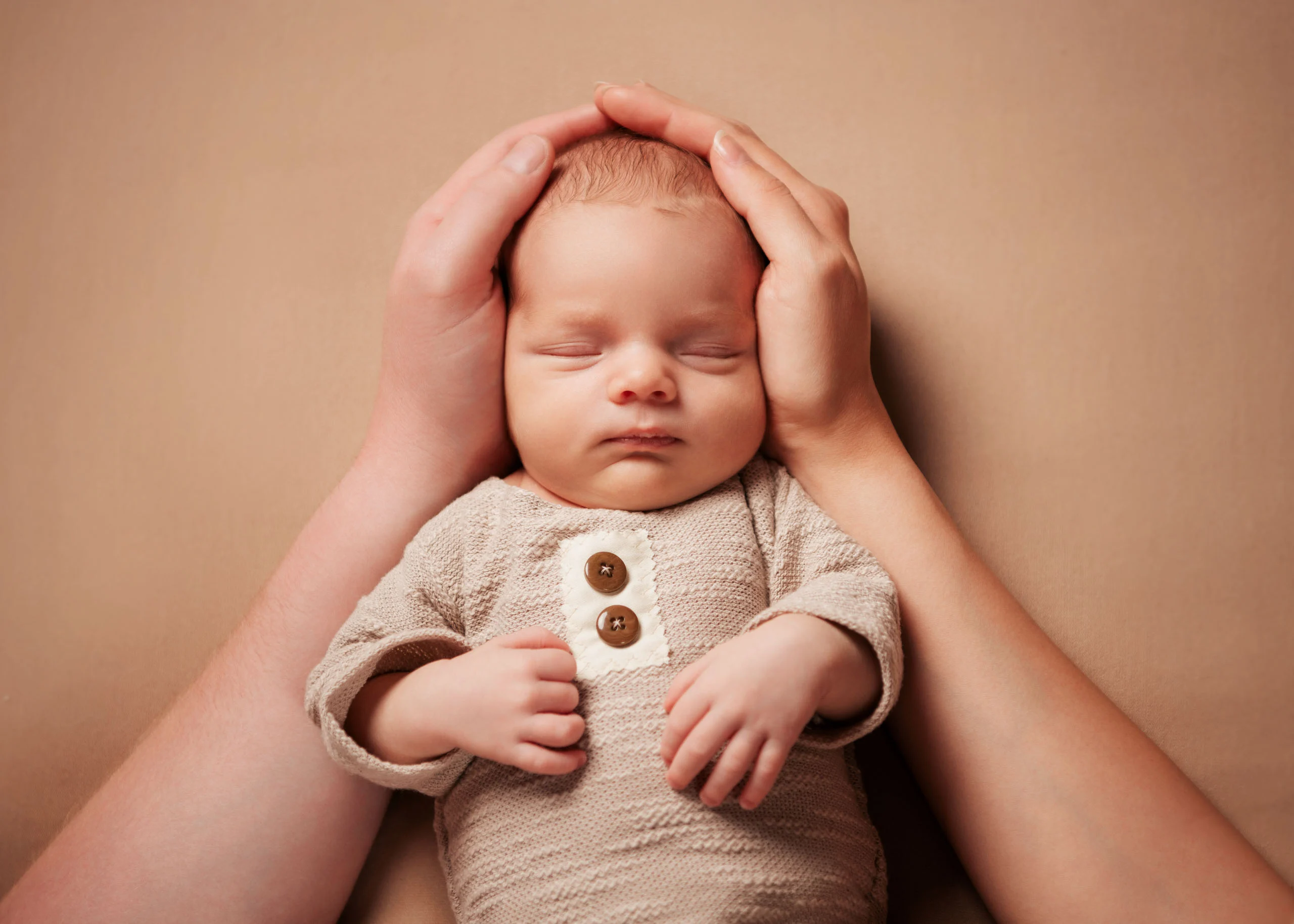 Babyfotos Neugeborene Fotogalerie 066 | Peter Lauritis Photography Hände halten den Kopf eines schlafenden Neugeborenen im Strickbody