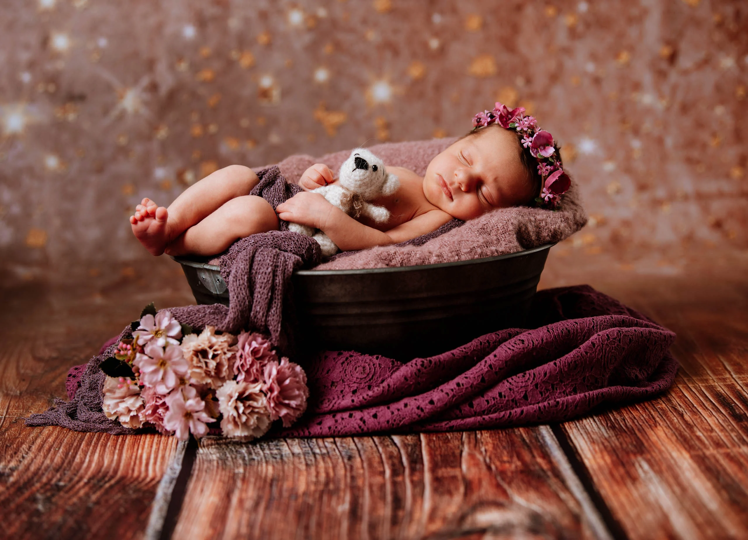 Babyfotos Neugeborene Fotogalerie 072 | Peter Lauritis Photography Schlafendes Neugeborenes mit Blumenkranz und kleinem Teddy in einer Schale vor Glitzerhintergrund