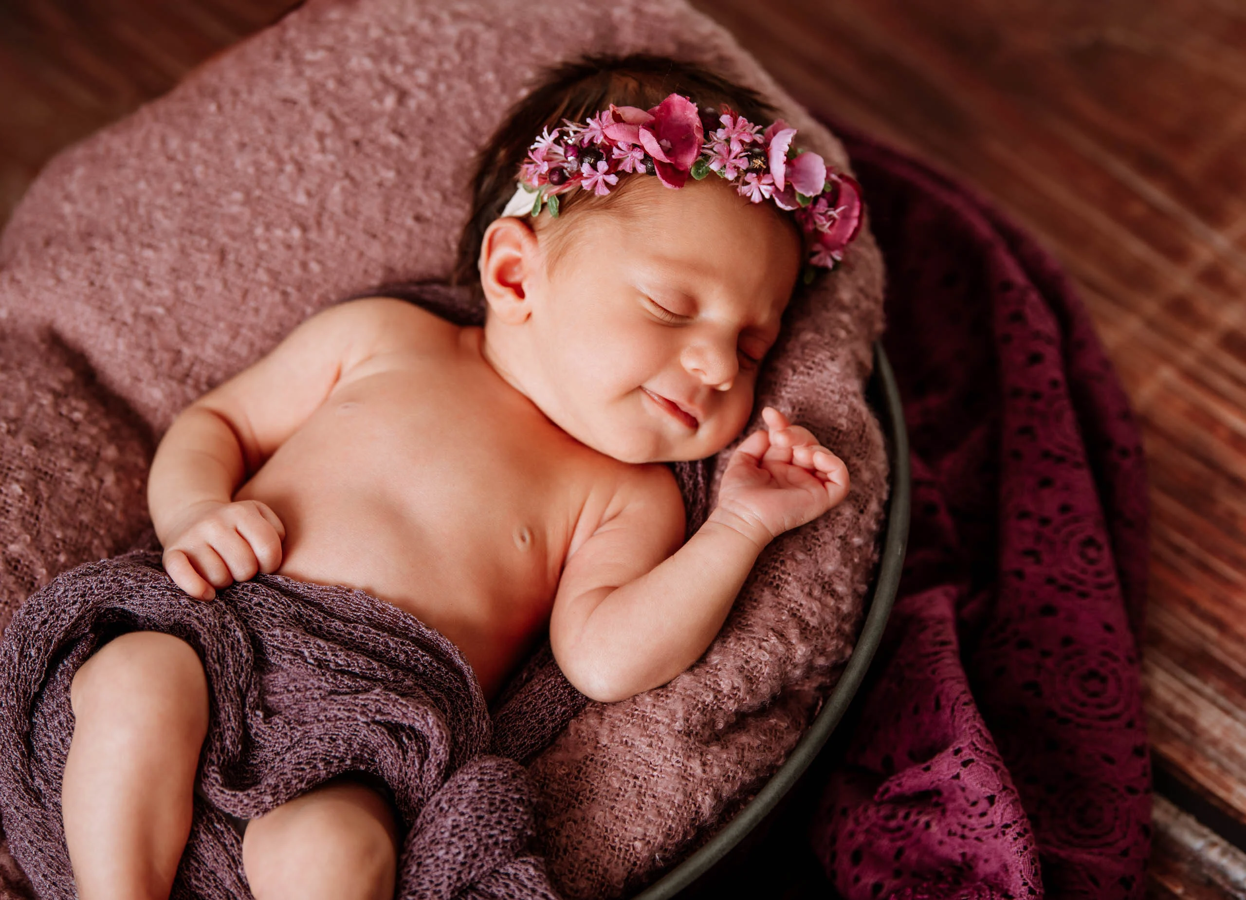 Babyfotos Neugeborene Fotogalerie 073 | Peter Lauritis Photography Lächelndes schlafendes Neugeborenes mit pinkem Blumenkranz auf lila Decke