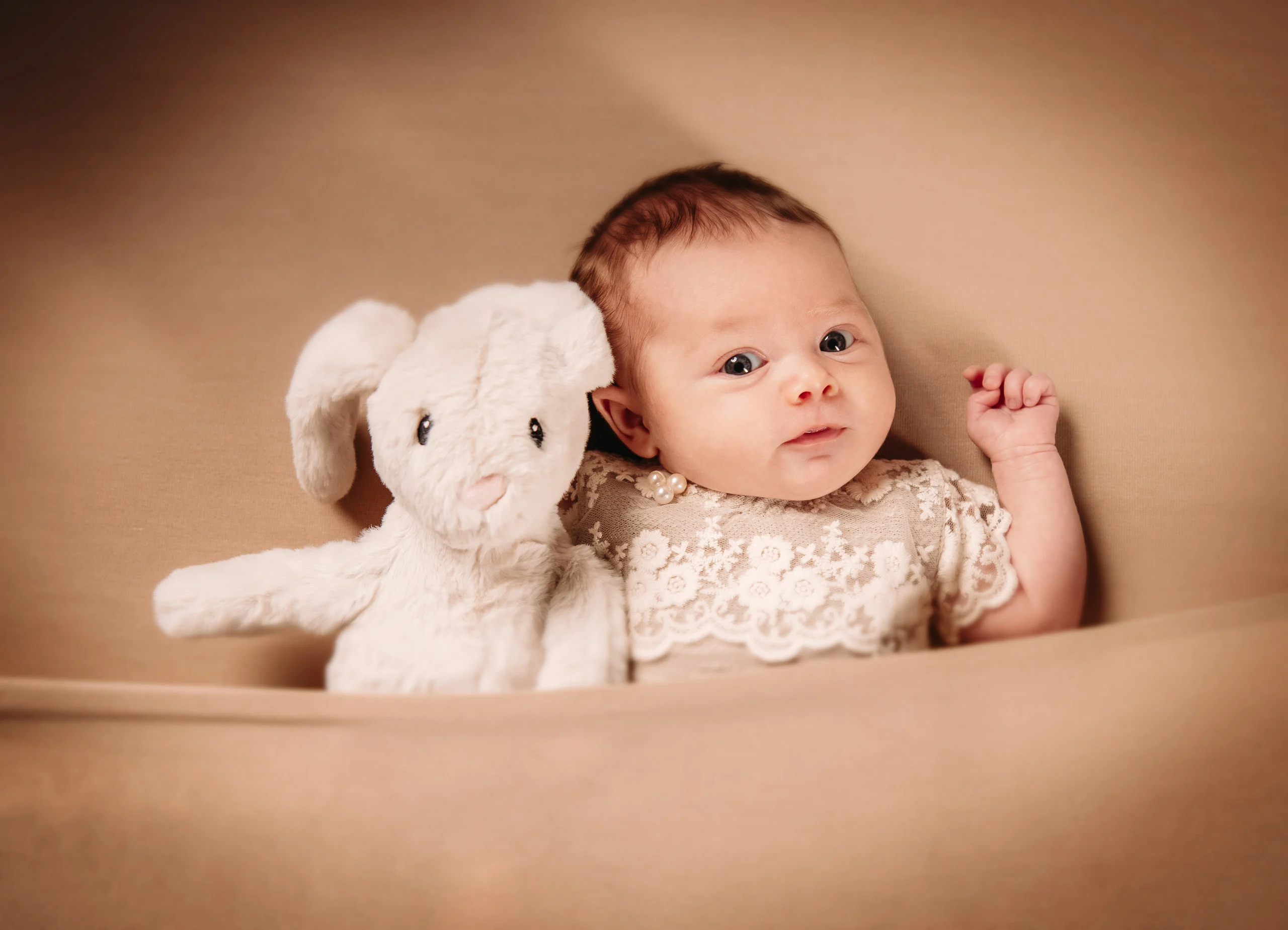Babyfotos Neugeborene Fotogalerie 084 | Peter Lauritis Photography Baby liegt neben einem weißen Plüschhasen auf beigem Stoff