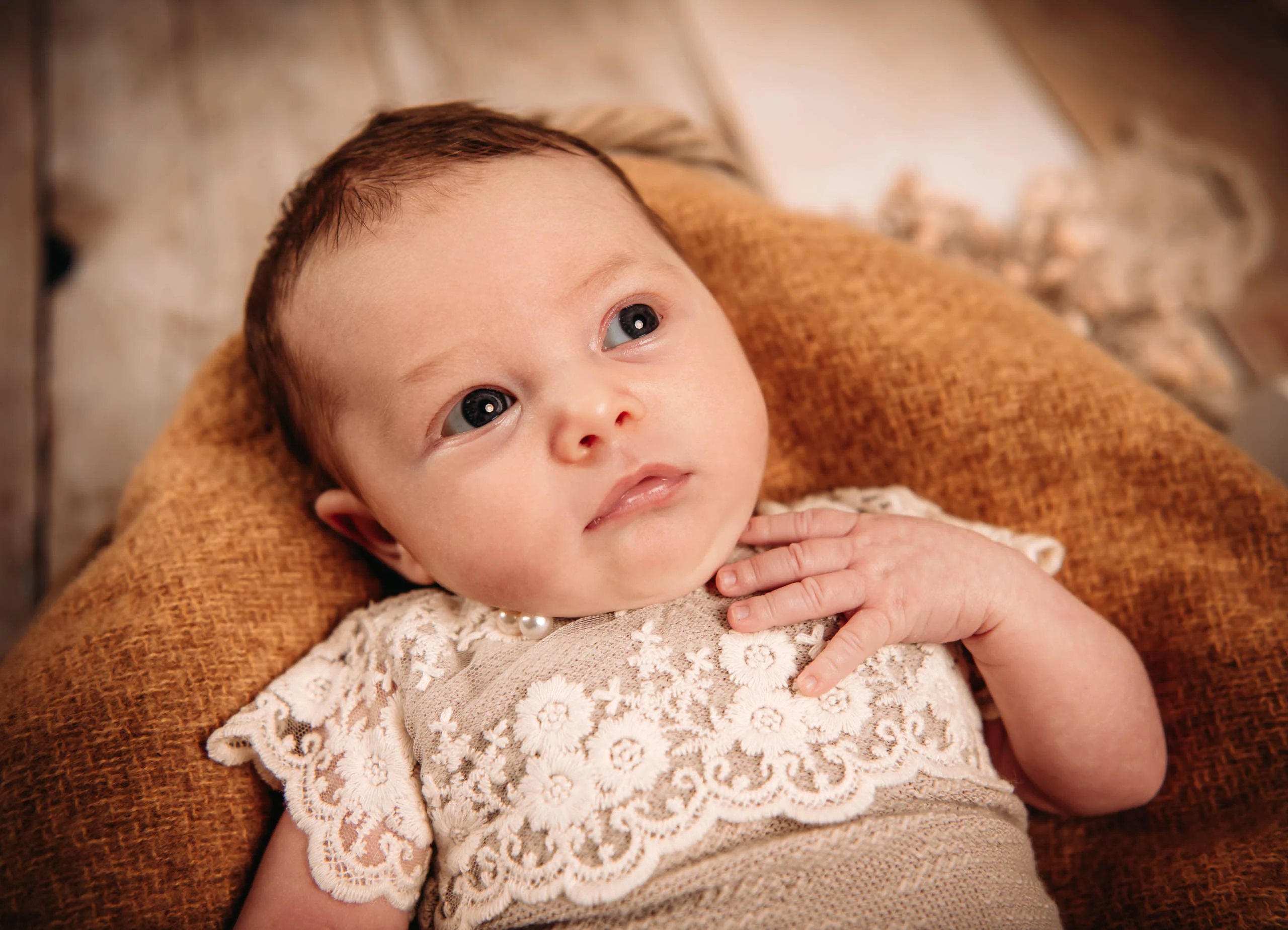 Babyfotos Neugeborene Fotogalerie 085 | Peter Lauritis Photography Baby im Spitzenbody liegt wach auf einem ockerfarbenen Kissen