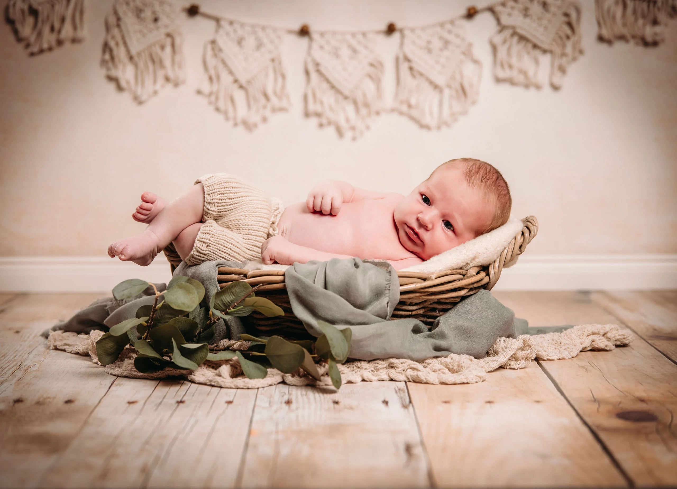 Babyfotos Neugeborene Fotogalerie 086 | Peter Lauritis Photography Neugeborenes liegt wach im Korb mit grünen Blättern vor Makramee