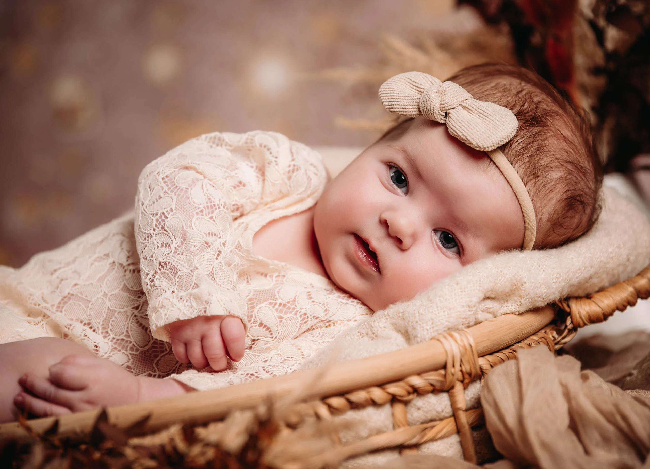 Babyfotos Neugeborene Fotogalerie 089 | Peter Lauritis Photography Baby mit Schleifen-Haarband liegt im Korb und schaut in die Kamera