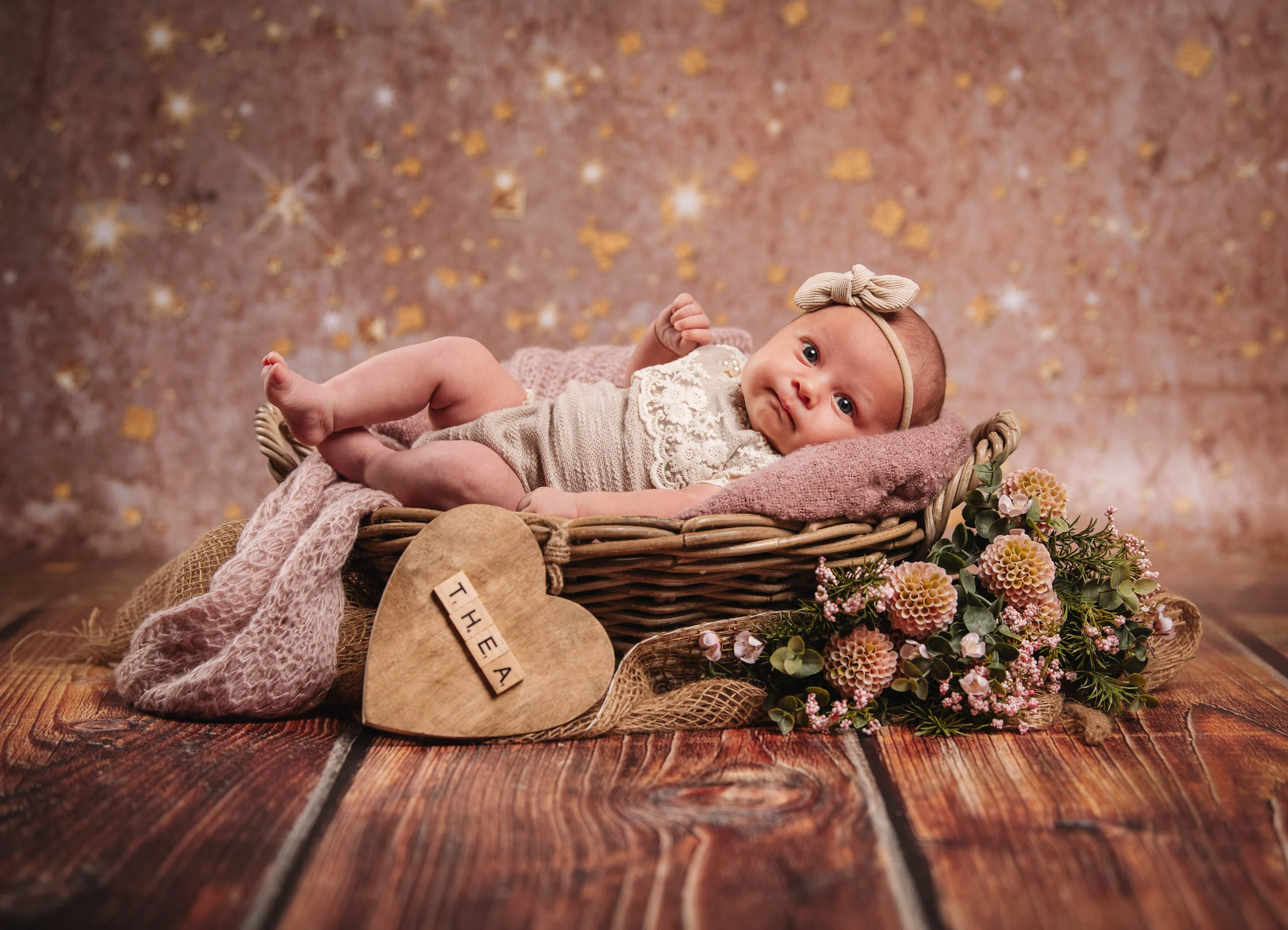Babyfotos Neugeborene Fotogalerie 091 | Peter Lauritis Photography Baby im Korb vor Glitzerhintergrund, davor ein Holzherz mit Namen und Blumen