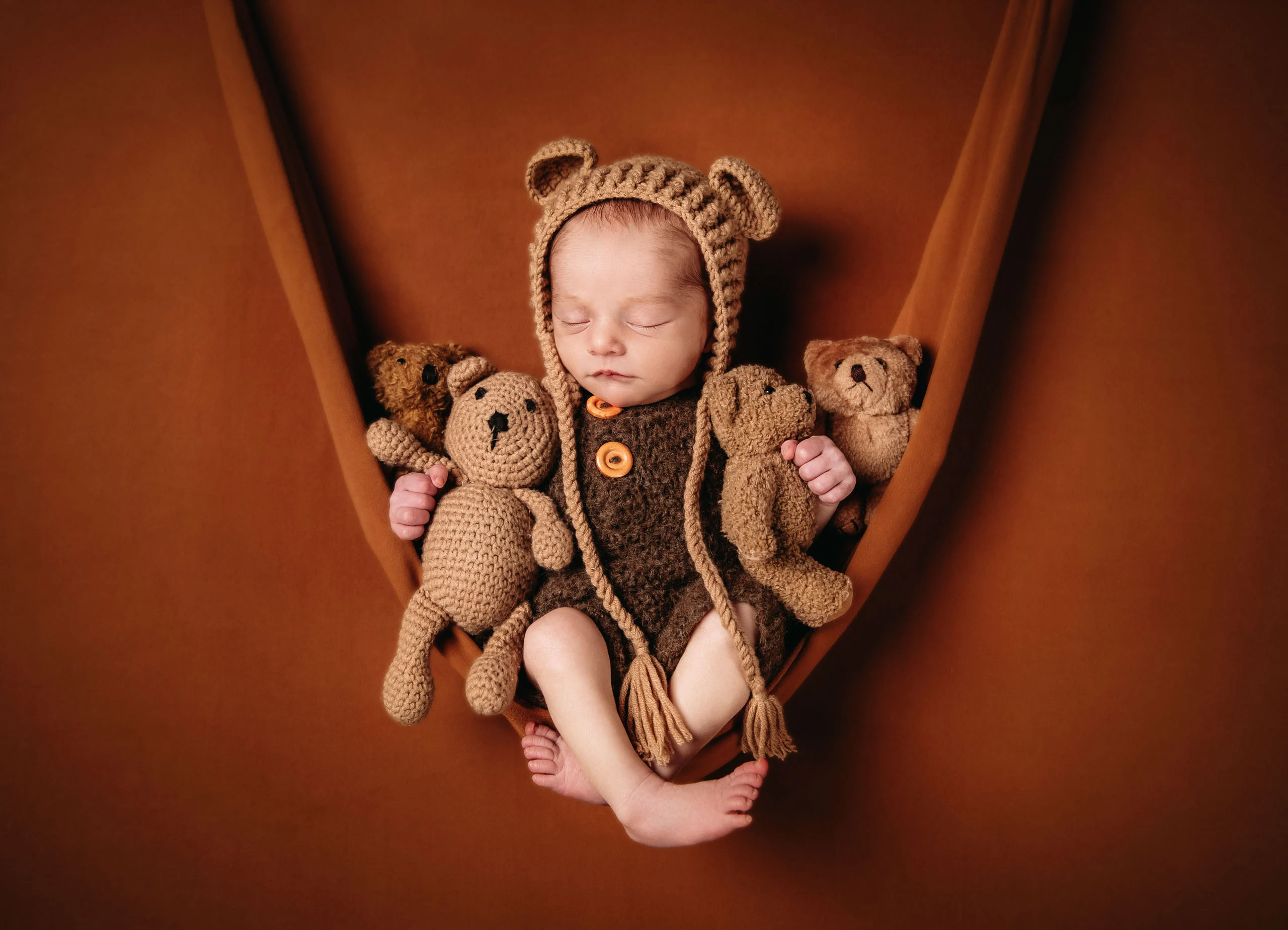 Babyfotos Neugeborene Fotogalerie 093 | Peter Lauritis Photography Neugeborenes mit gehäkelter Bärenmütze und Teddys in einer Stoffhängematte