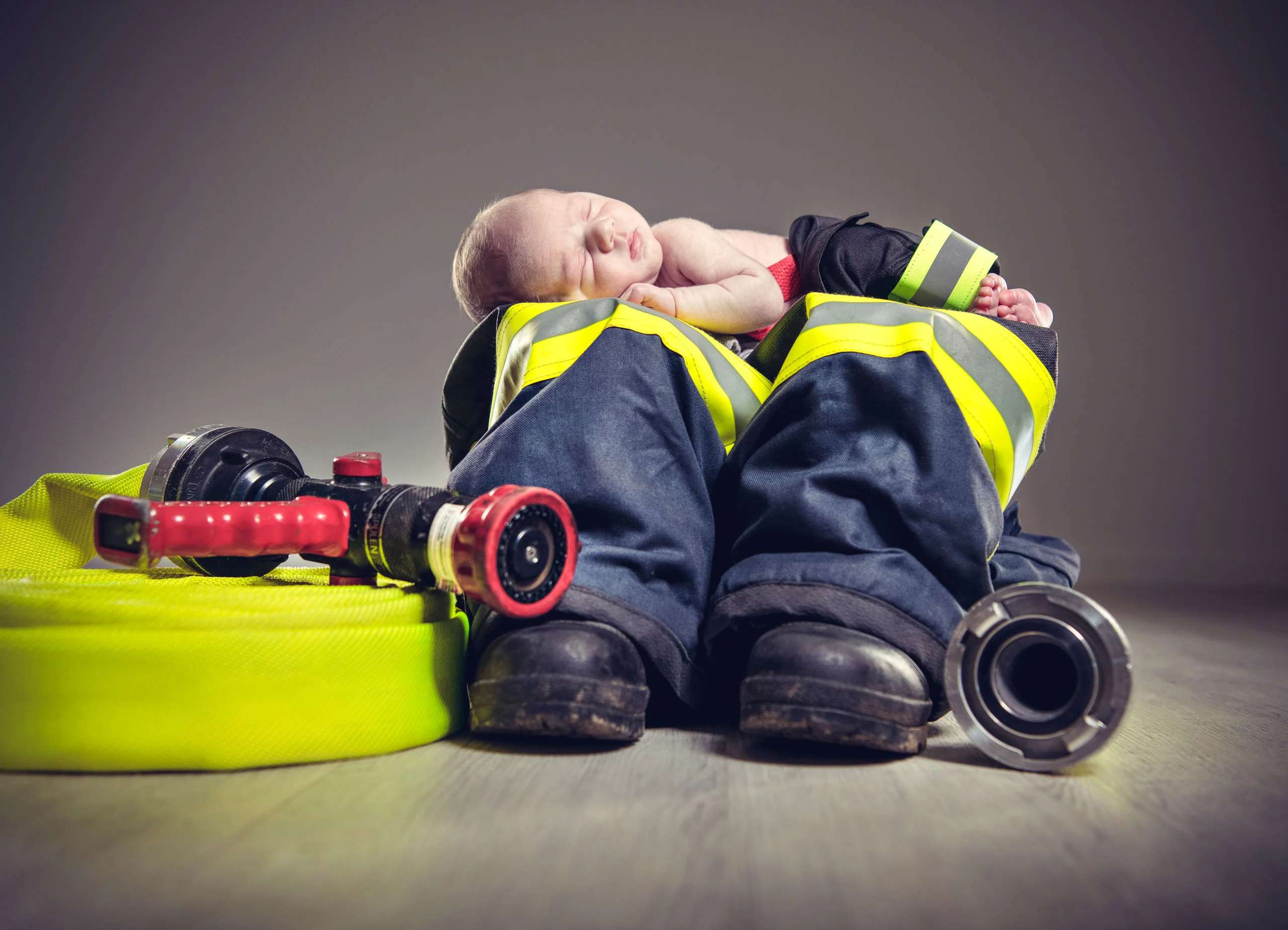 Babyfotos Neugeborene Fotogalerie 099 | Peter Lauritis Photography Neugeborenes schläft auf Feuerwehrstiefeln und Einsatzhose neben einem Schlauch