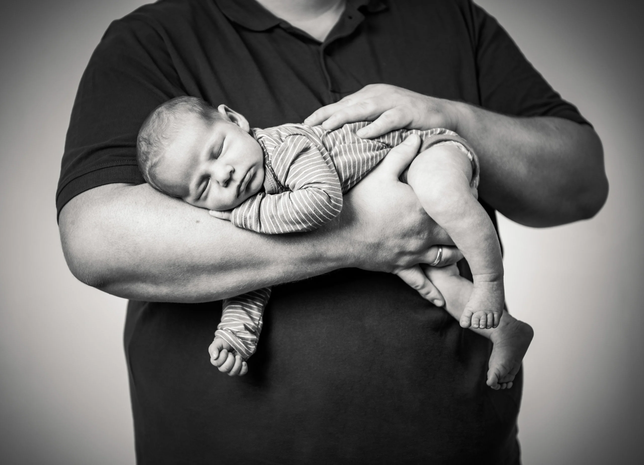 Babyfotos Neugeborene Fotogalerie 106 | Peter Lauritis Photography Schwarzweißfoto: Mann trägt das schlafende Neugeborene auf dem Unterarm