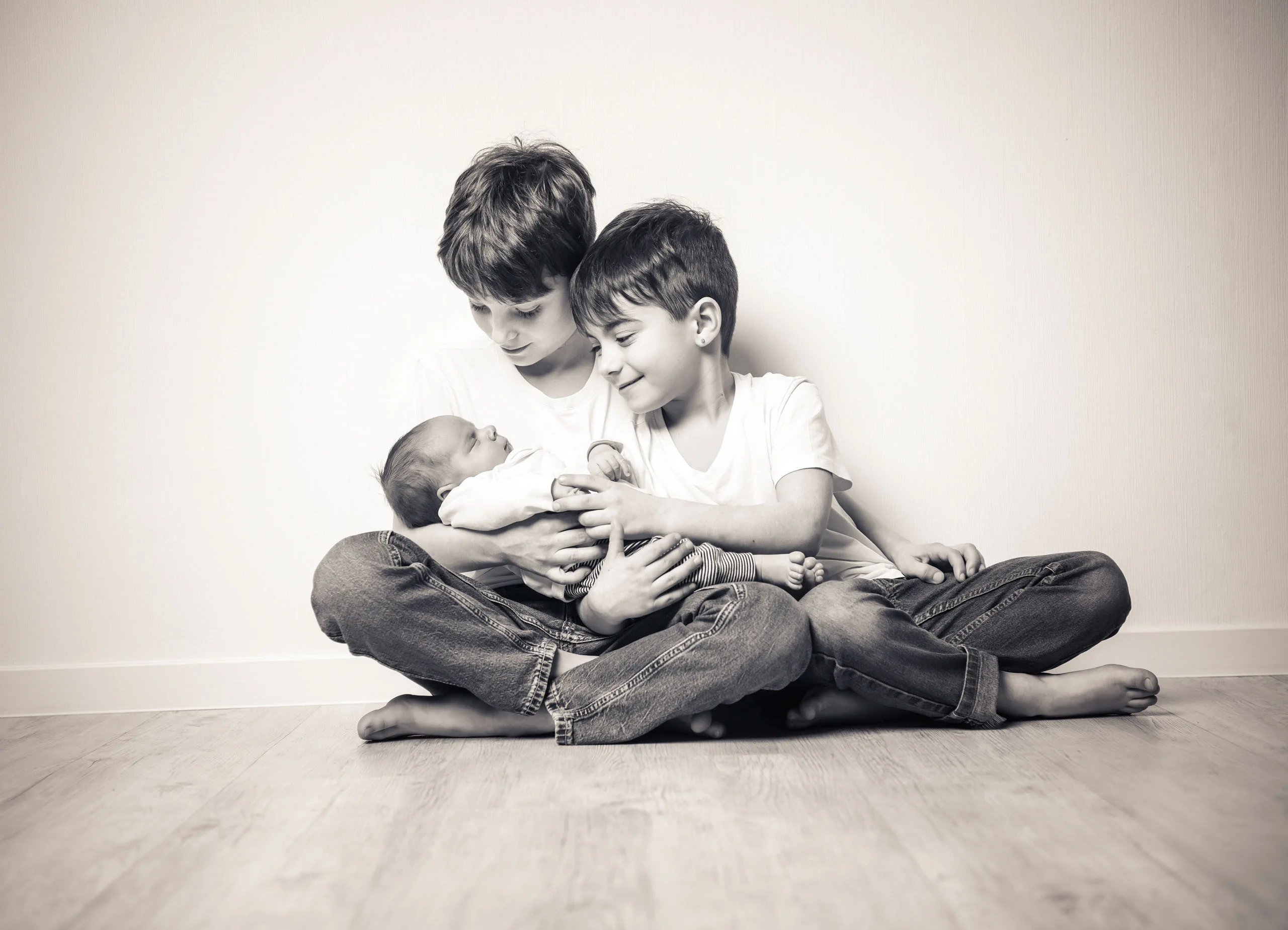 Babyfotos Neugeborene Fotogalerie 107 | Peter Lauritis Photography Zwei Jungen sitzen im Schneidersitz und halten gemeinsam das Neugeborene