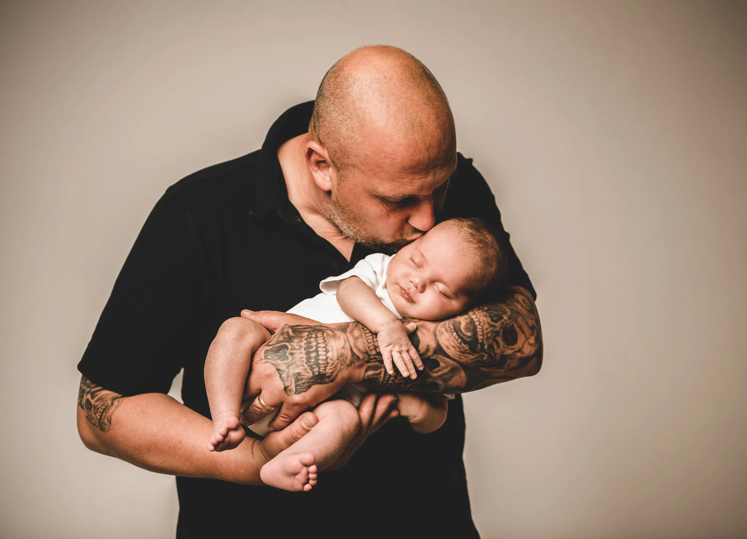 Babyfotos Neugeborene Fotogalerie 111 | Peter Lauritis Photography Tätowierter Mann im schwarzen Shirt küsst das Neugeborene auf seinem Arm