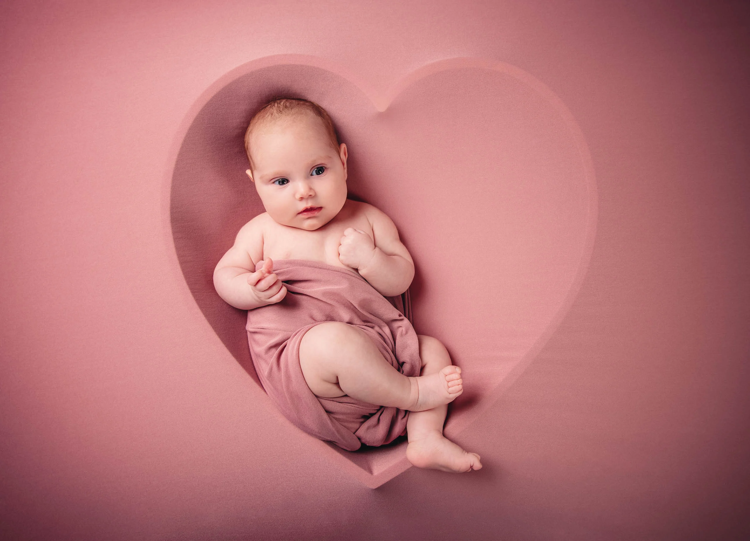 Babyfotos Neugeborene Fotogalerie 113 | Peter Lauritis Photography Baby liegt in einer herzförmigen Mulde auf rosa Hintergrund