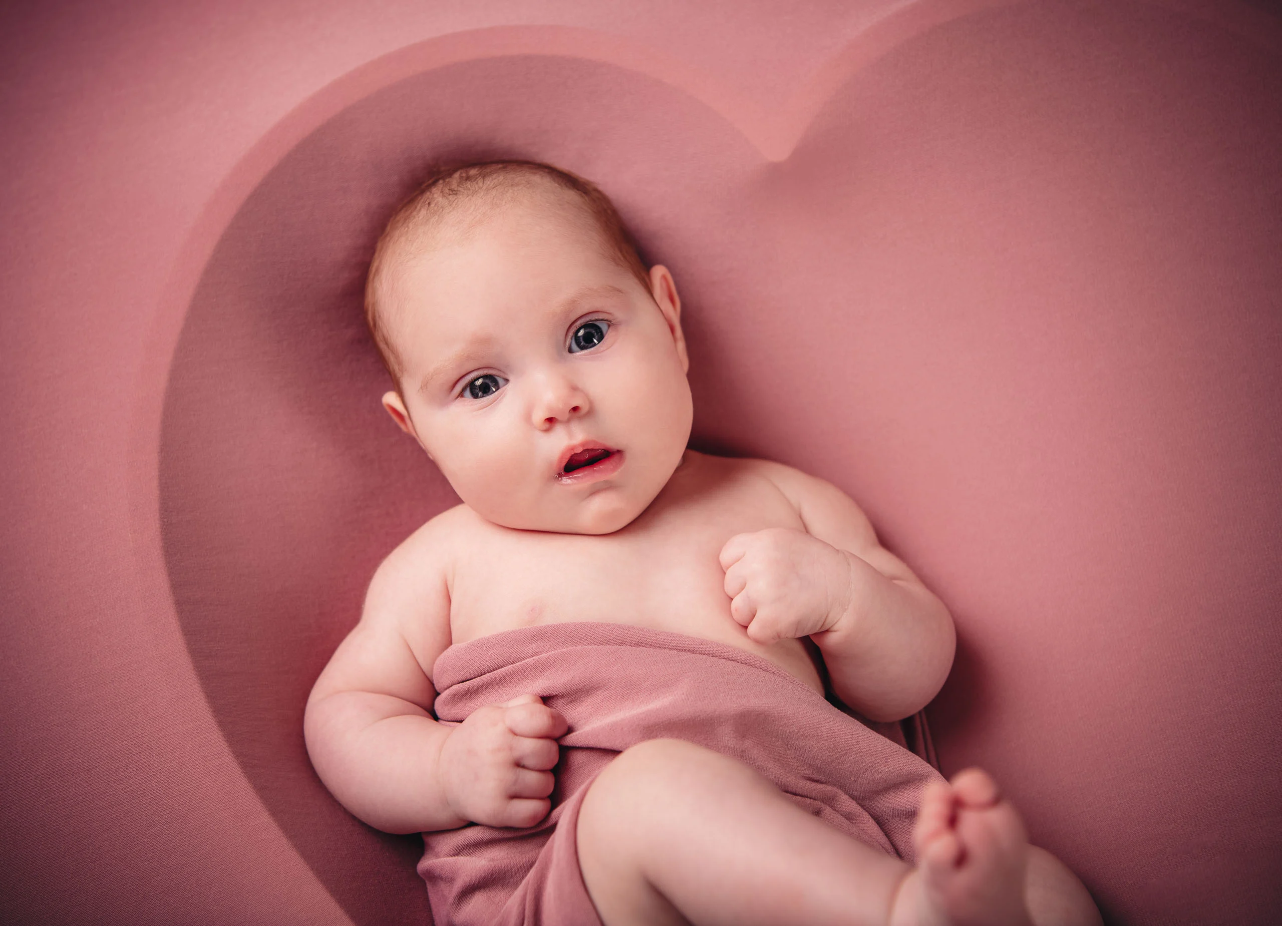 Babyfotos Neugeborene Fotogalerie 114 | Peter Lauritis Photography Baby mit rosa Tuch blickt aus einer Herzmulde in die Kamera
