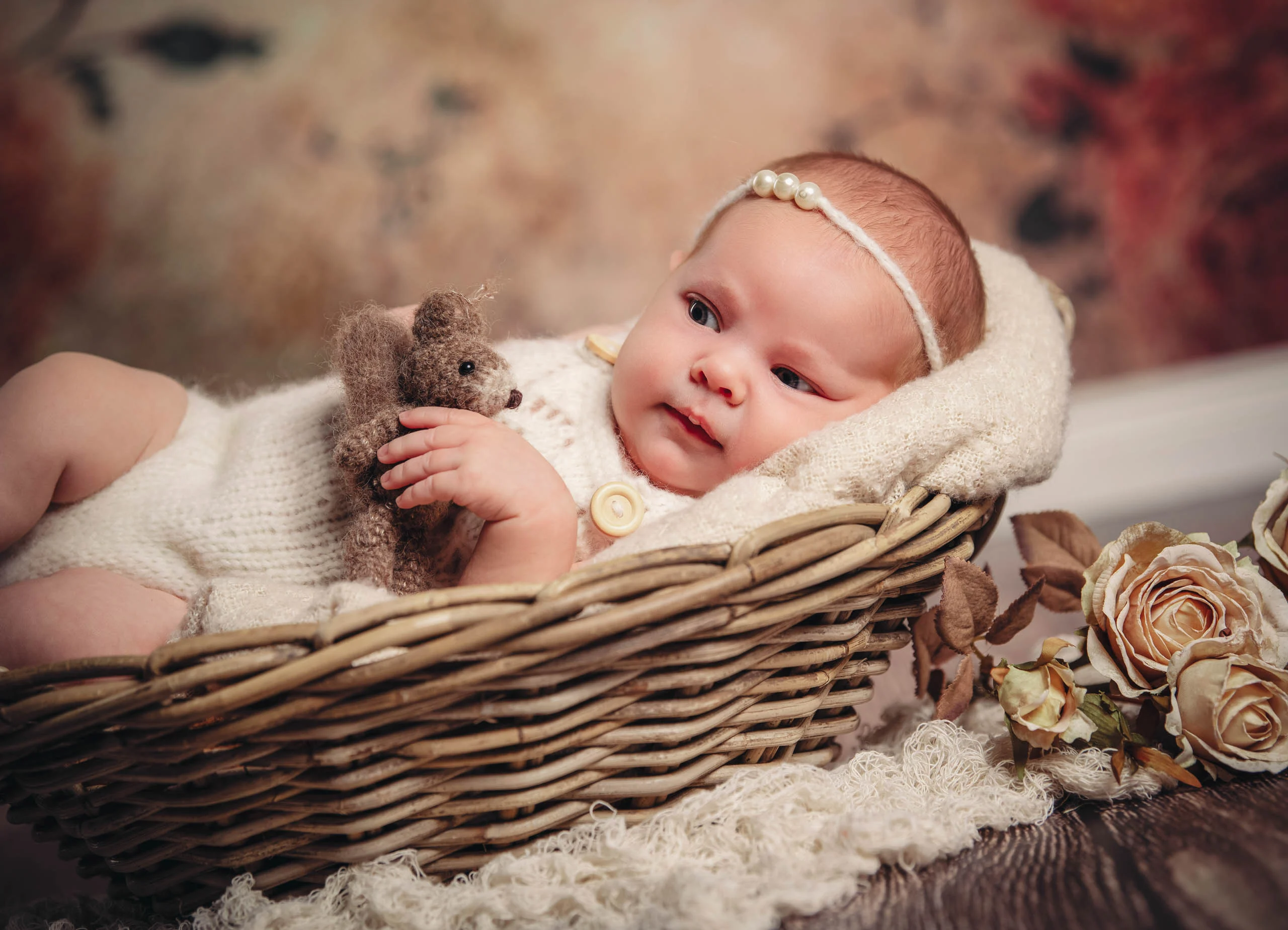 Babyfotos Neugeborene Fotogalerie 116 | Peter Lauritis Photography Baby mit Haarband hält einen Teddy im Korb neben Rosen