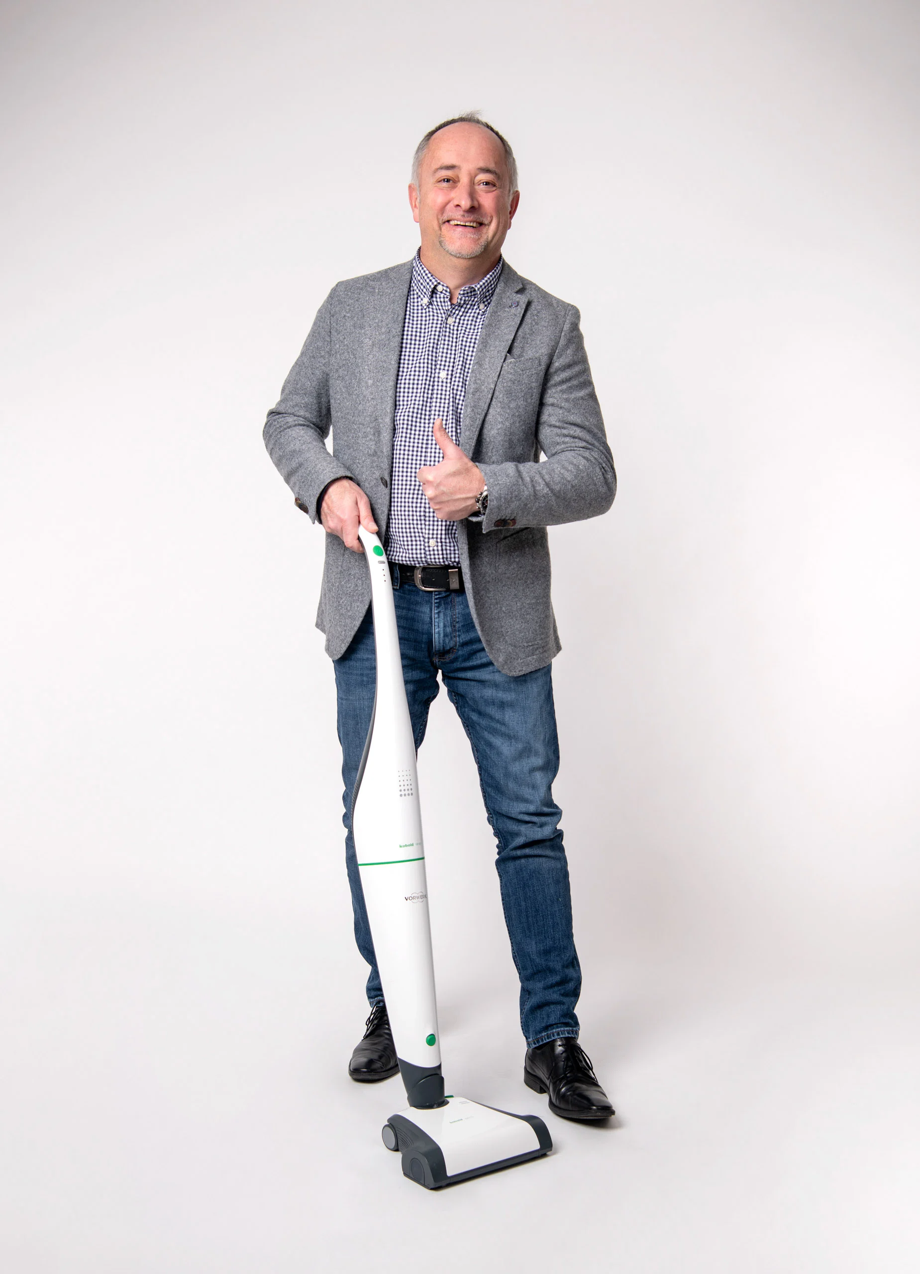 Business Portraits Fotogalerie 013 | Peter Lauritis Photography Mann im grauen Sakko hält einen Bodenstaubsauger und zeigt den Daumen hoch