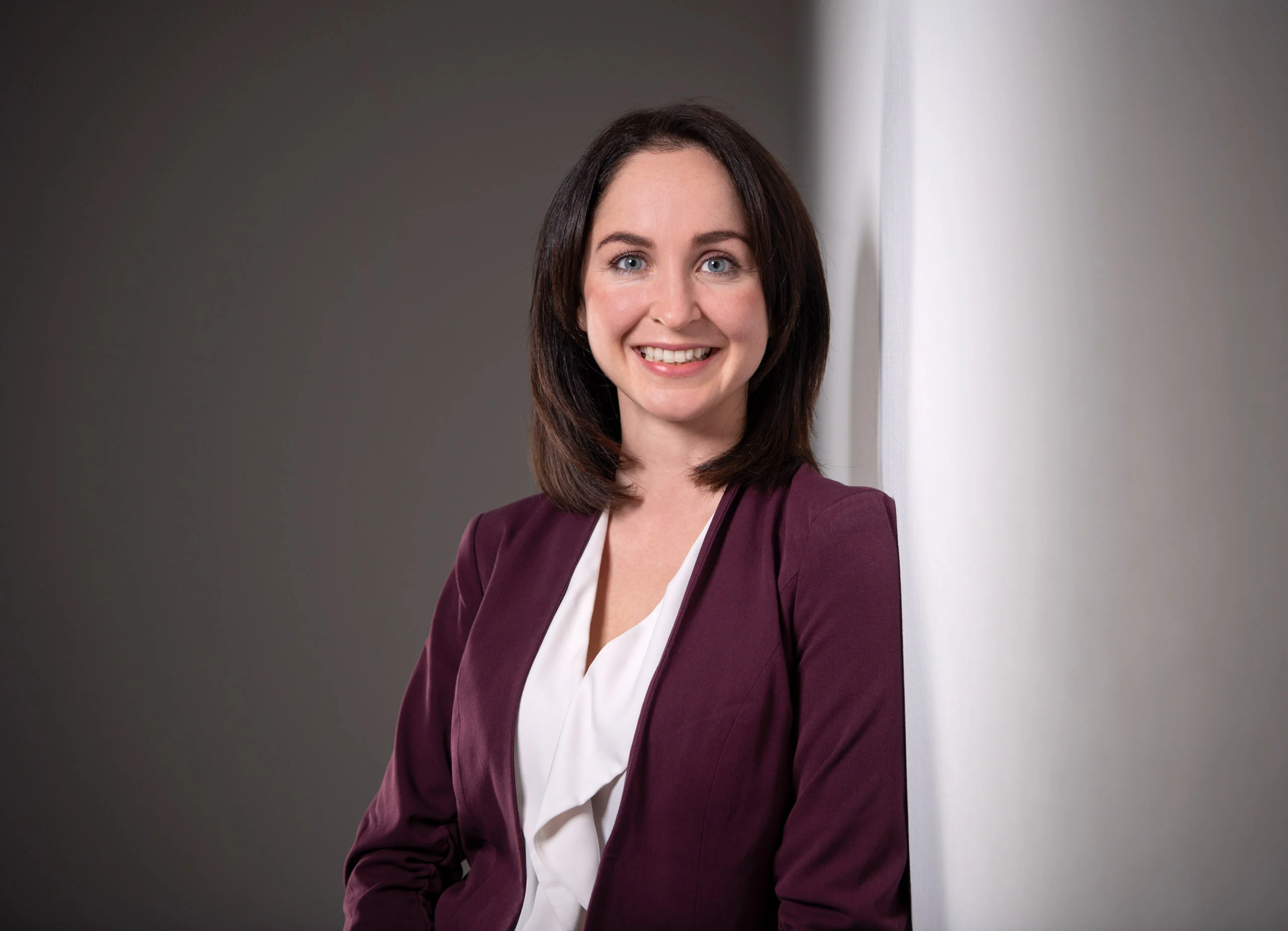 Business Portraits Fotogalerie 016 | Peter Lauritis Photography Lachende Frau im weinroten Blazer lehnt an einer hellen Wand