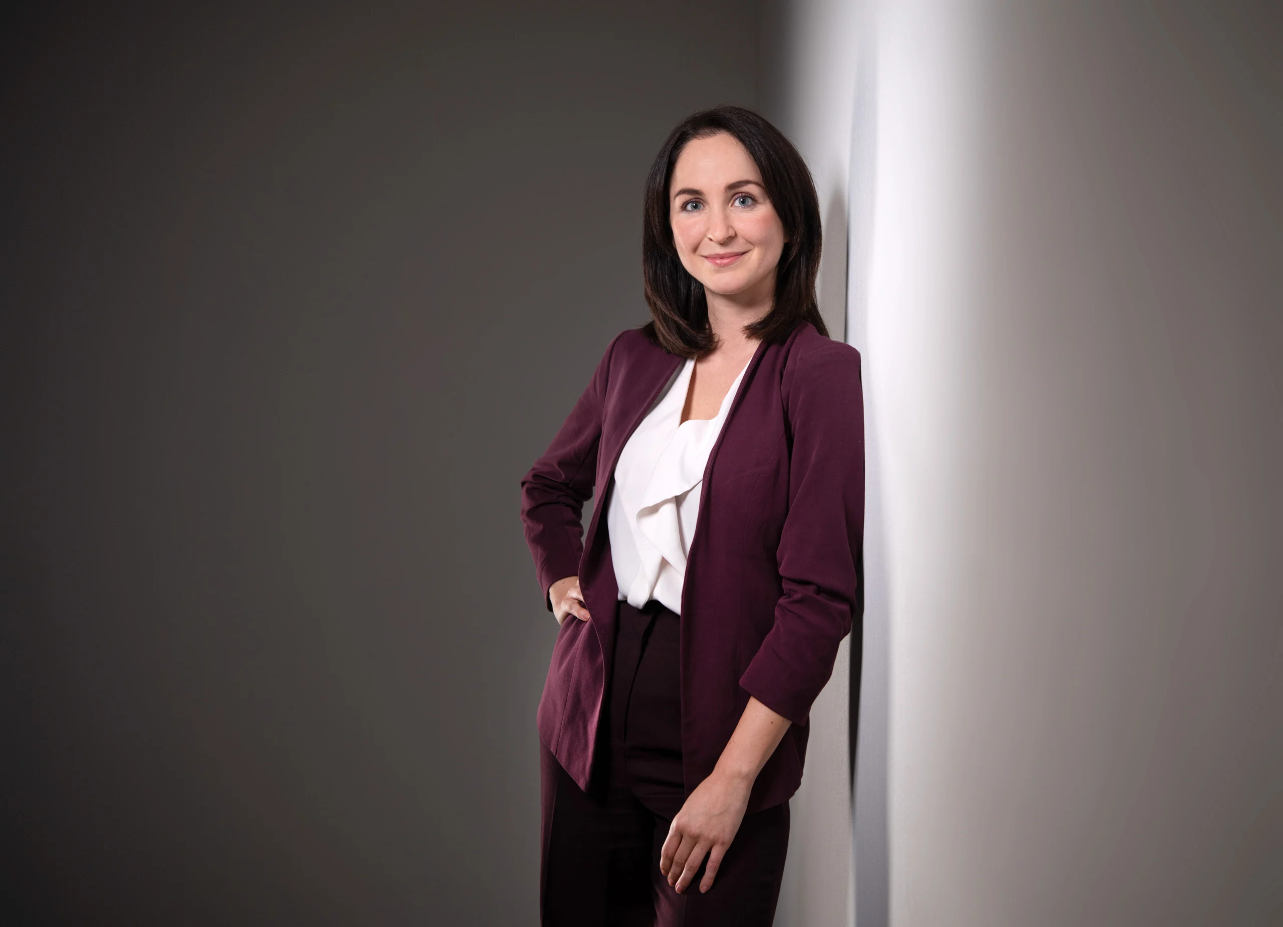 Business Portraits Fotogalerie 018 | Peter Lauritis Photography Frau im weinroten Blazer steht mit der Hand in der Hüfte an einer Wand