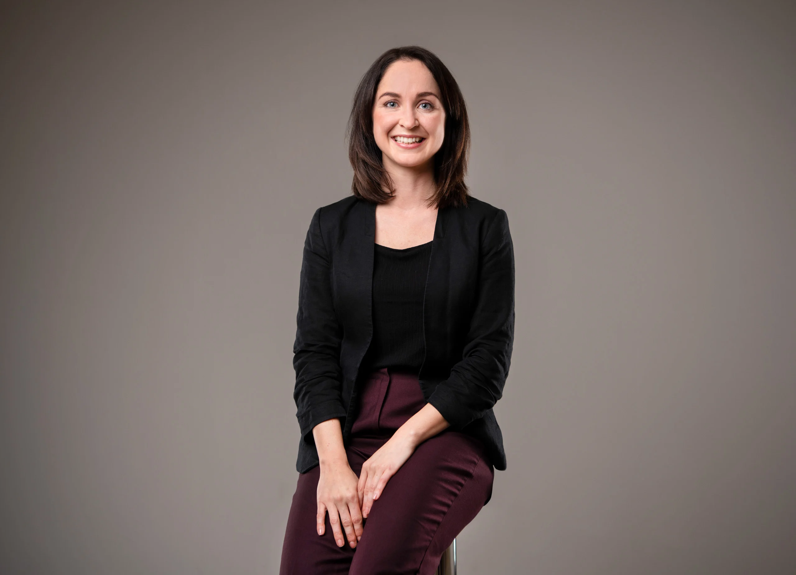 Business Portraits Fotogalerie 019 | Peter Lauritis Photography Frau im schwarzen Blazer sitzt lächelnd auf einem Barhocker